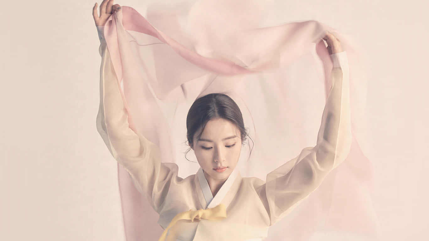 桌布 壁紙 — 一位穿著傳統服飾的寧靜女性，在柔和的中性背景前優雅地舉起一條飄逸的粉紅色絲巾。