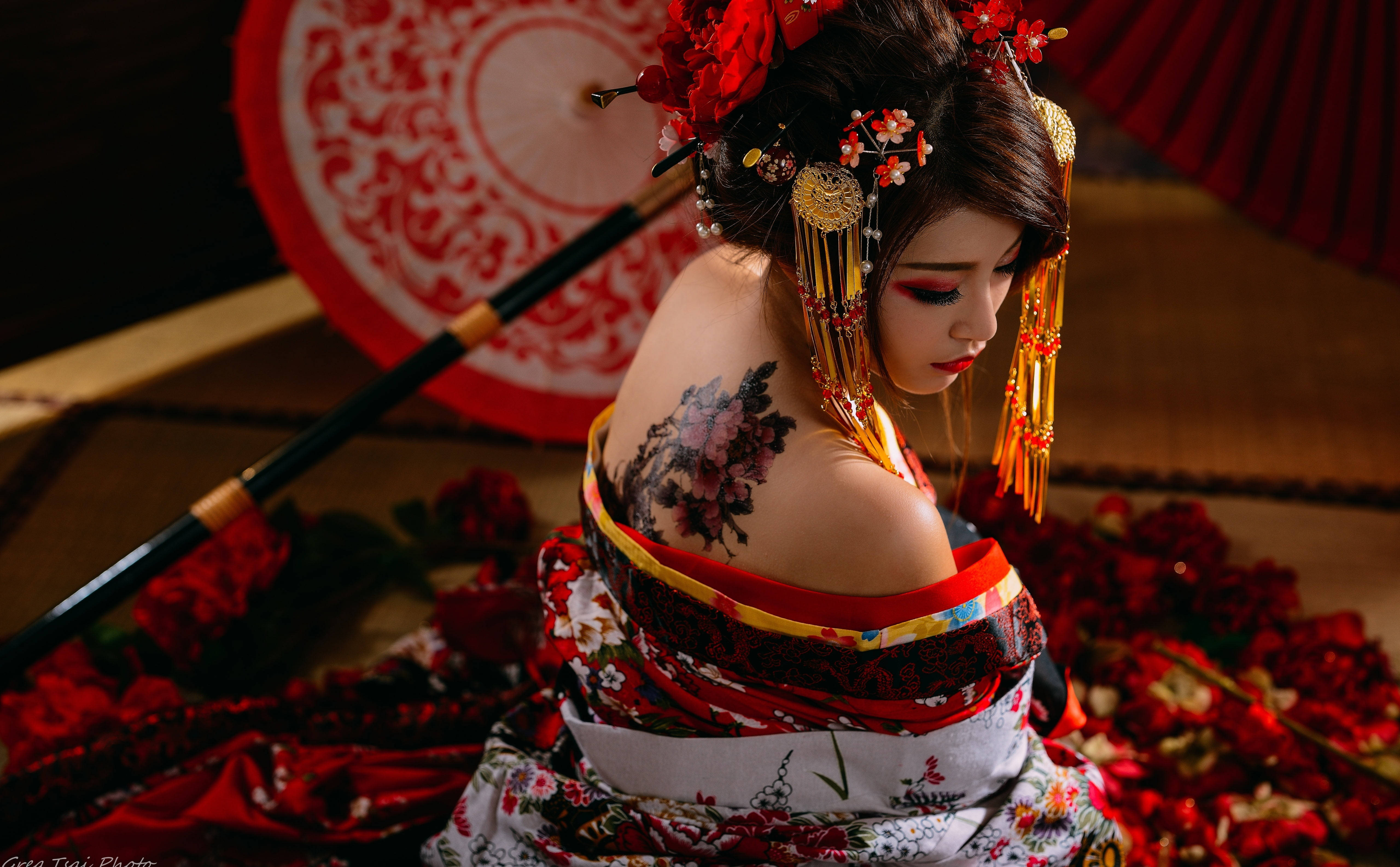 Tattoo 桌布 壁紙 — 一位穿著傳統紅白和服、帶有花卉刺青的藝妓，在散落的紅色花瓣和華麗的傘中低頭凝視。