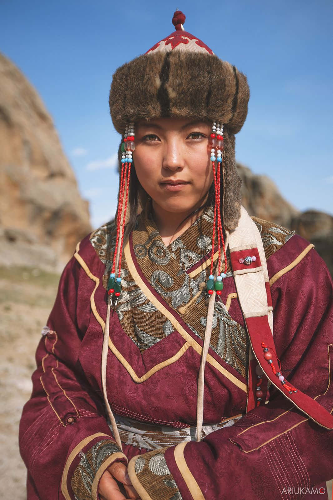 Woman 桌布 壁紙 — 一位穿著傳統蒙古服飾的年輕女性，在晴朗藍天下以岩石山脈為背景站立。