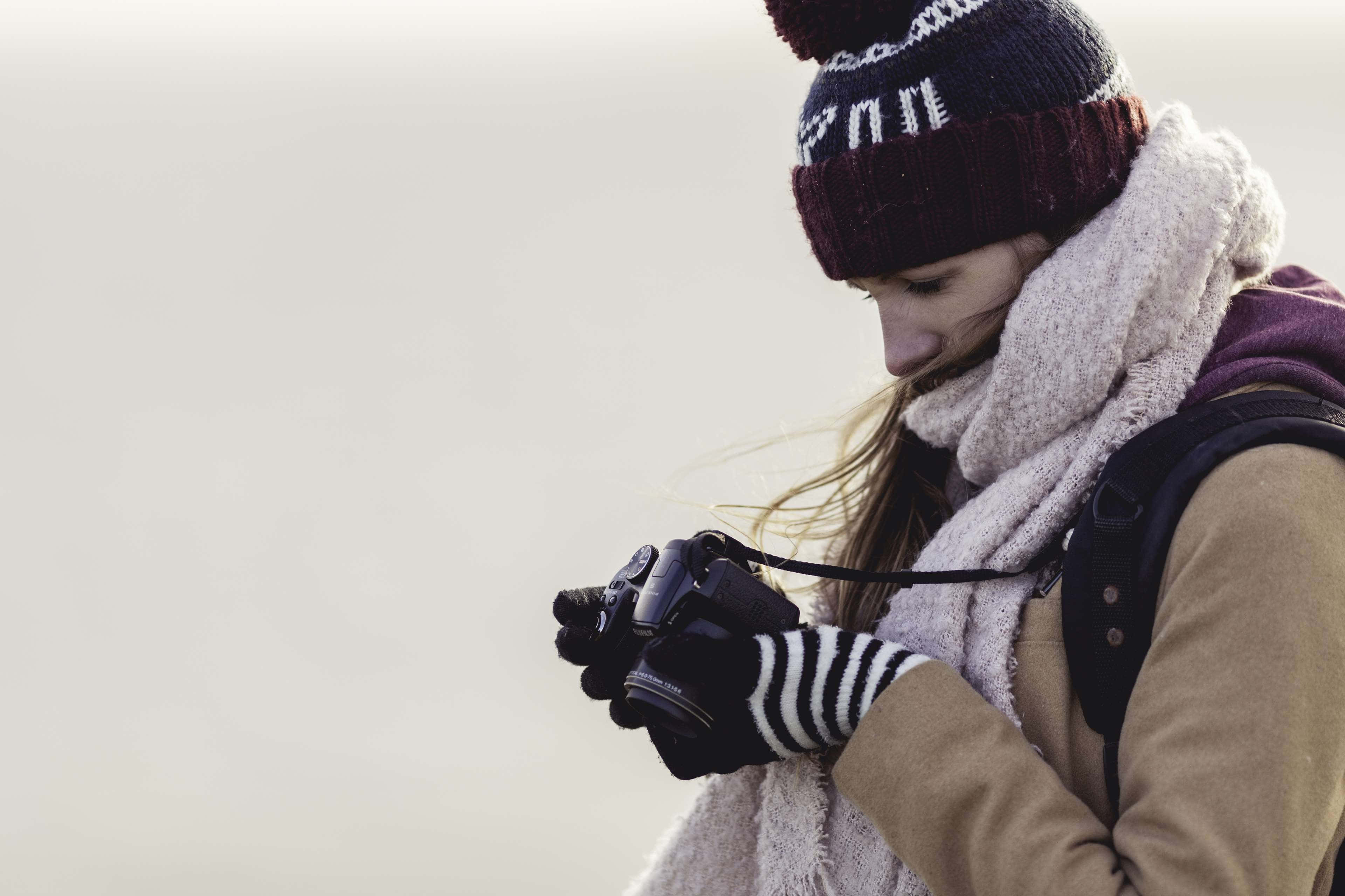 Winter Fashion 桌布 壁紙 — 一位穿著冬季裝備的女性，在柔和的多雲天空下，專注地拿著相機。