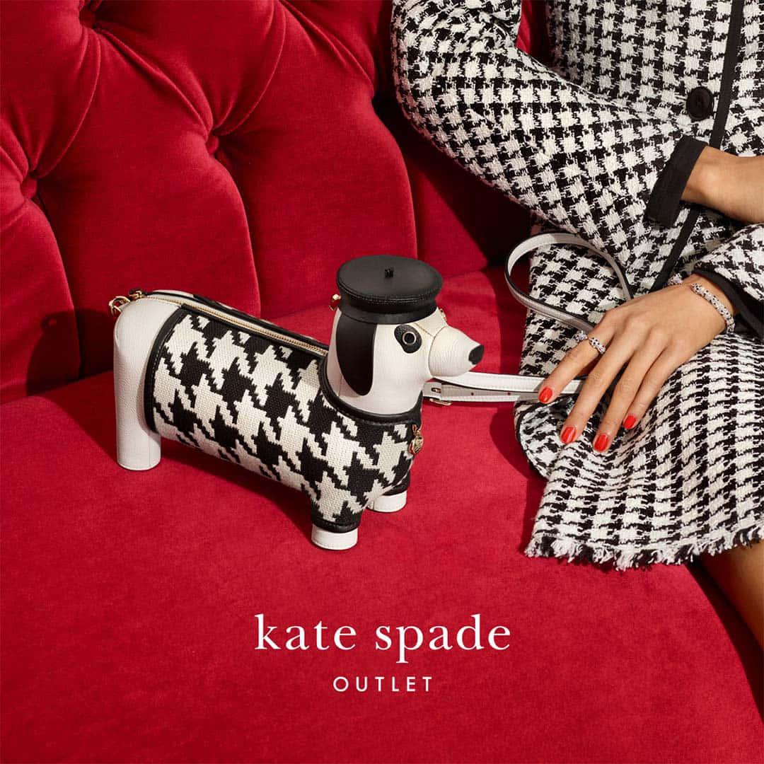 Kate Spade 桌布 壁紙 — 一位穿著千鳥格大衣的人坐在一張毛絨紅色沙發上，旁邊放著一個相配的臘腸犬形狀手袋。