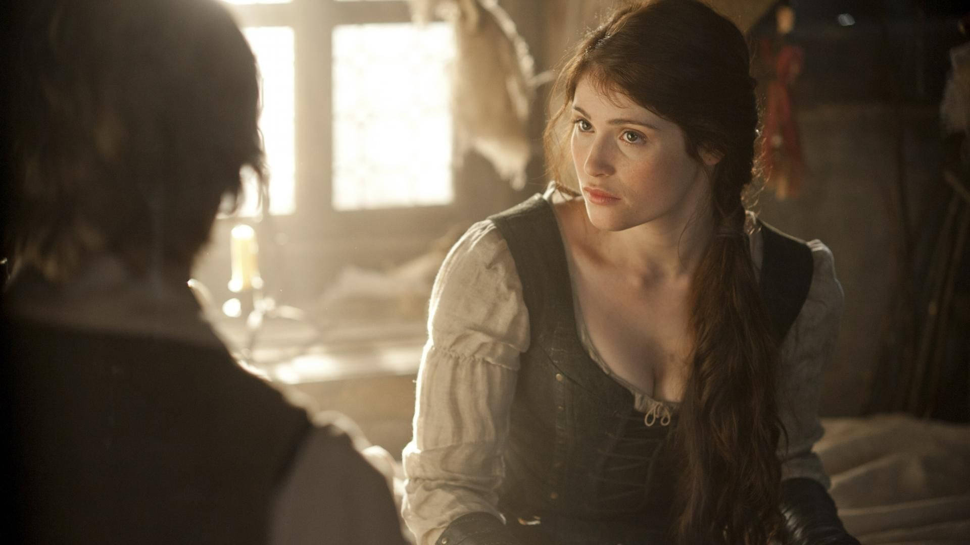 Gemma Arterton 桌布 壁紙 — 一位穿著古裝的女子在溫暖光線的鄉村風格房間內，透過窗戶灑進柔和陽光，專注地凝視另一個人。