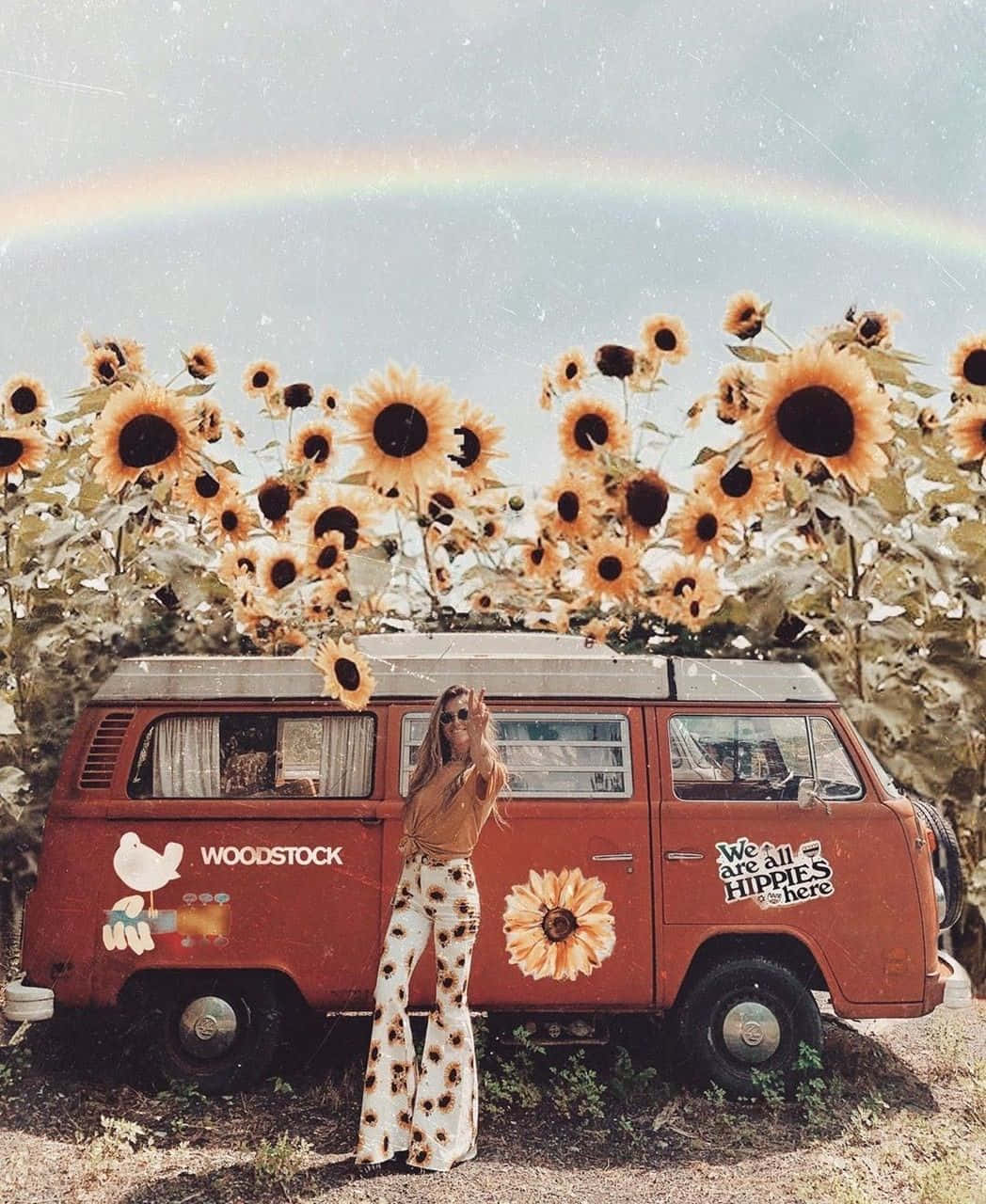 彩虹 桌布 壁紙 — 一位穿著向日葵印花褲子的女性站在一輛貼有 'Woodstock' 和 'We are all Hippies here' 貼紙的復古紅色廂型車旁，周圍是彩虹下高高的向日葵田。