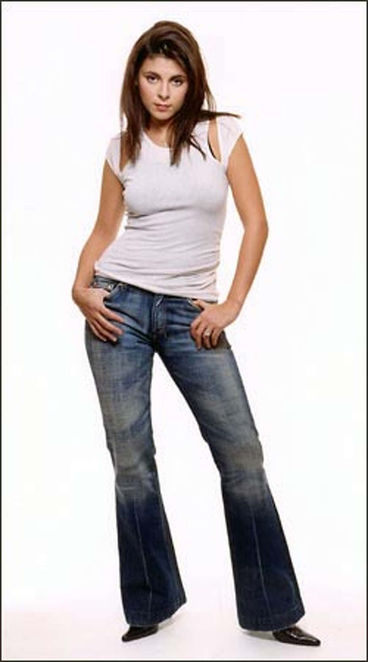Jamie Lynn Sigler 桌布 壁紙 — 一位穿著喇叭牛仔褲和白色上衣的女性在純白背景前自信地擺姿勢。