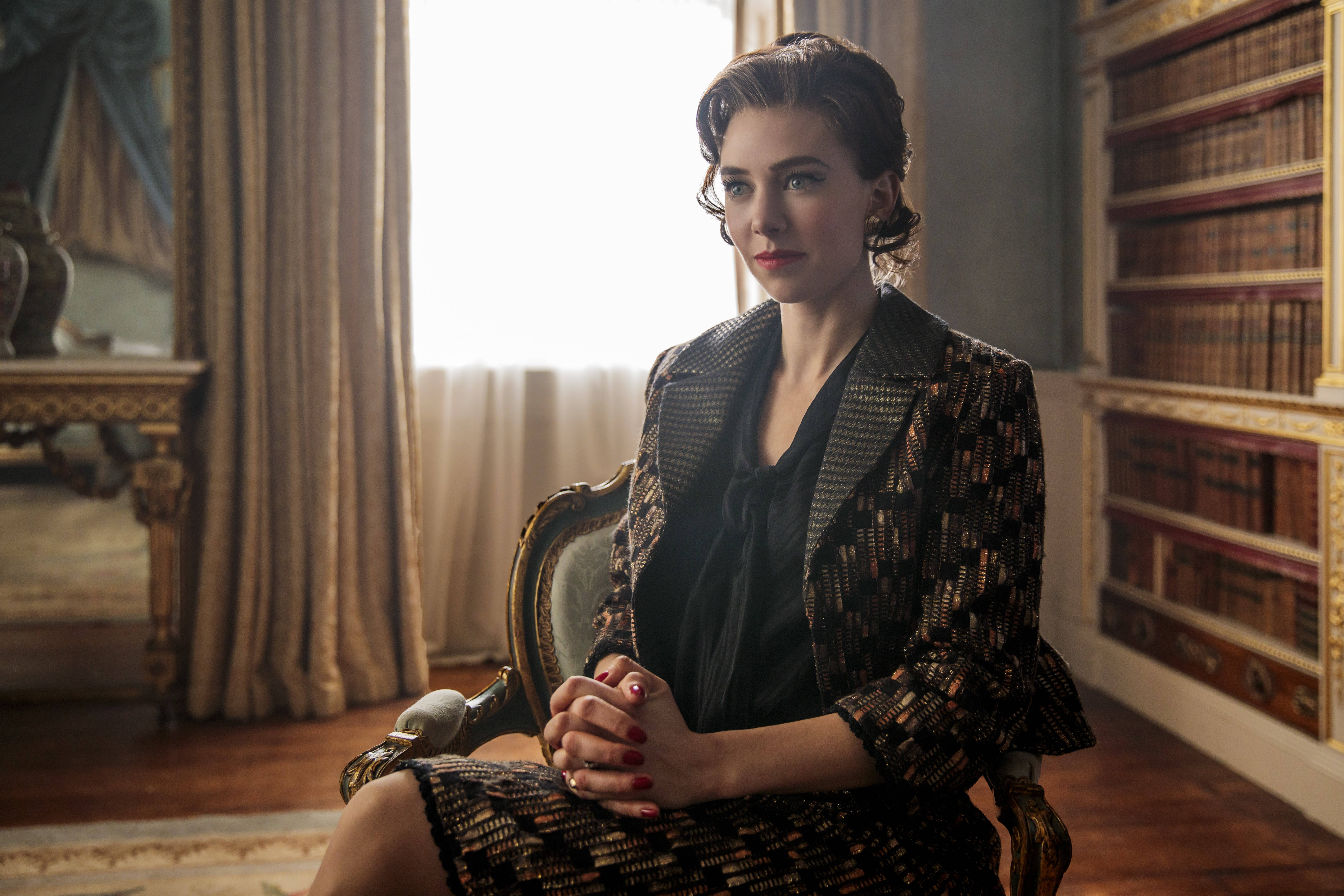 the crown 桌布 壁紙 — 一位穿著圖案西裝的優雅女士，在陽光充足、書架林立的圖書館中，端莊地坐在一張華麗的椅子上。