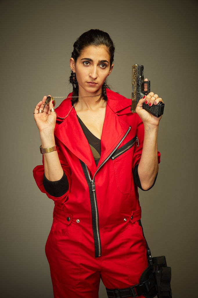 nairobi money heist 桌布 壁紙 — 一位穿著大膽紅色連身衣的女性，在灰色中性背景前，手持手槍和一顆子彈，神情嚴肅。