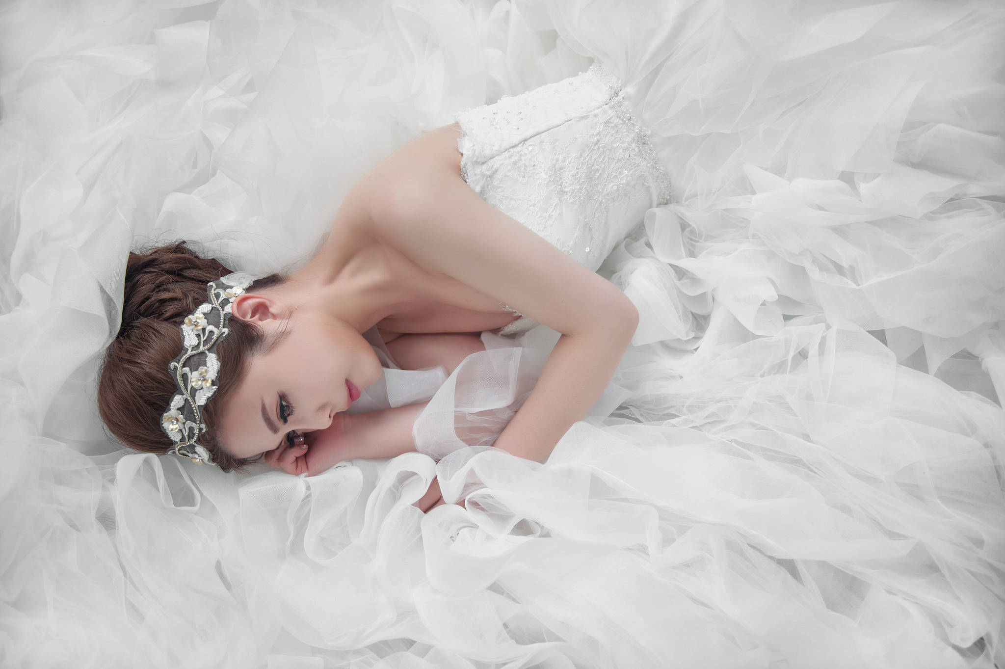 Wedding Aesthetic 桌布 壁紙 — 一位穿著寬大白色禮服的新娘，平靜地躺在如海洋般流動的薄紗布料上，頭戴花卉頭飾。