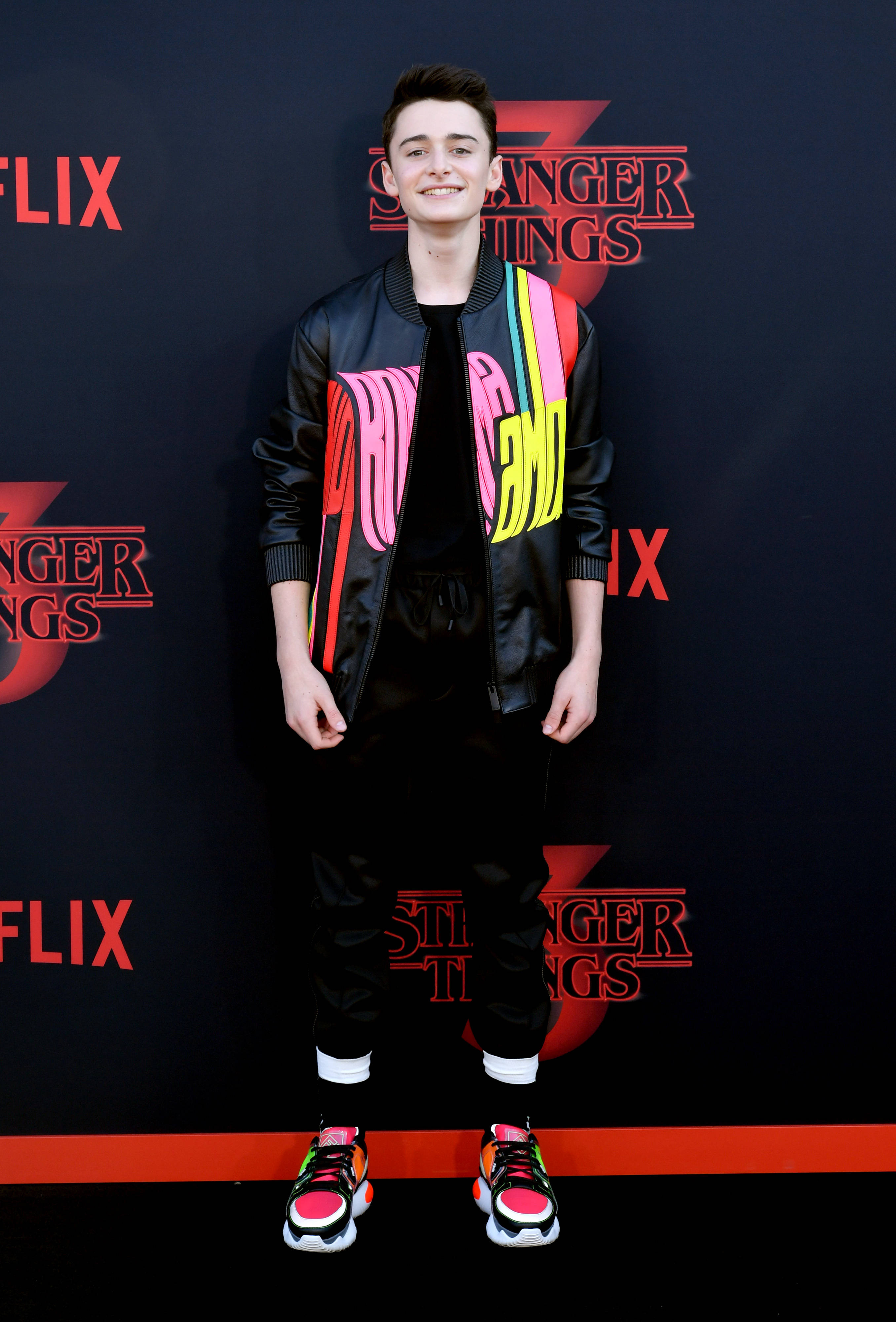 Netflix 桌布 壁紙 — 一位穿著彩色飛行員夾克和明亮運動鞋的年輕男子在 Netflix《怪奇物語》活動中微笑。