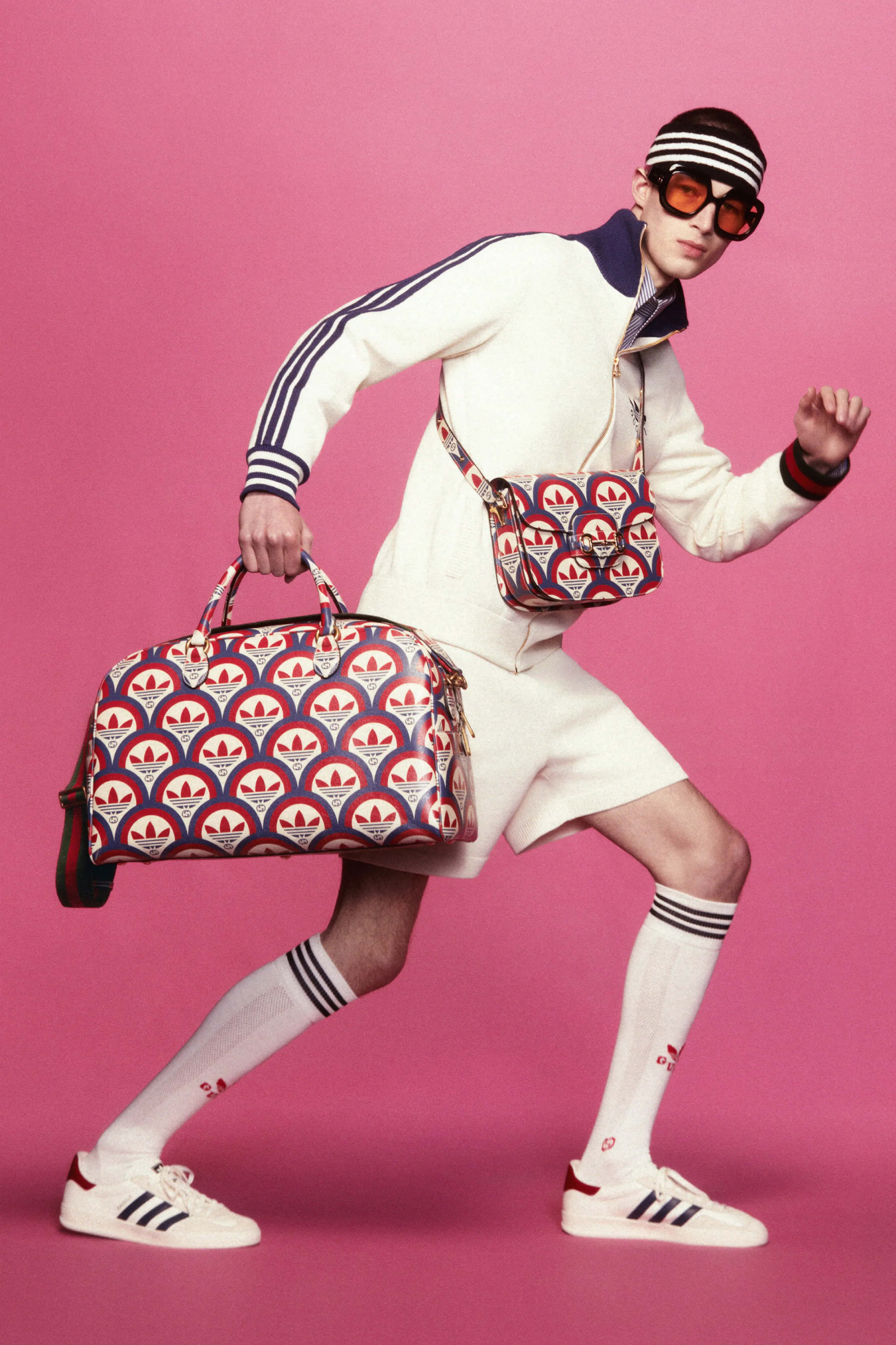 Gucci 桌布 壁紙 — 一位穿著復古Adidas裝備的模特兒在充滿活力的粉紅色工作室背景下動態擺姿勢，手持相配的圖案手提袋。