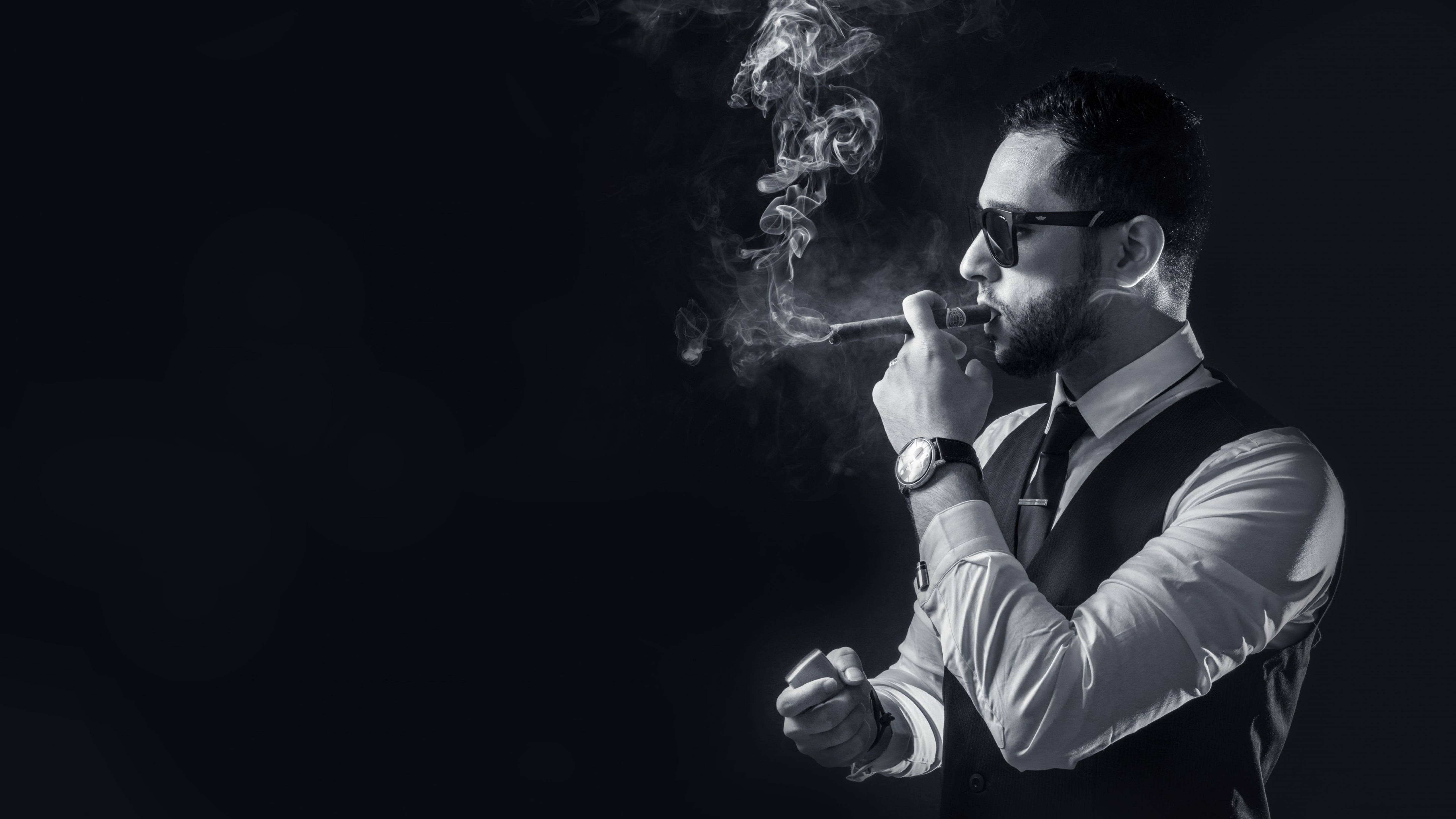 cigarettes 桌布 壁紙 — 一位穿著時尚、戴著太陽眼鏡的男士，在高對比度的黑白背景下，對著純黑背景吐煙。