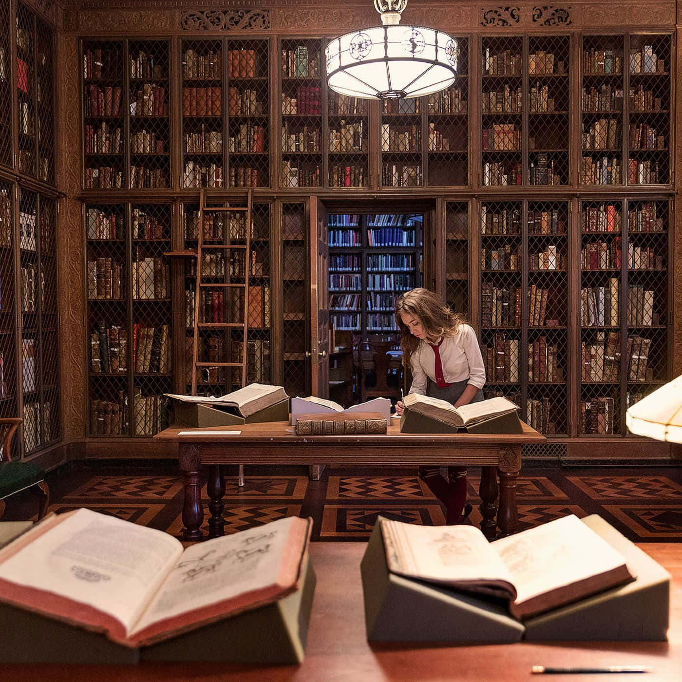 The Hogwarts Library 桌布 壁紙 — 一位穿著校服的年輕女子在一張木桌上研究古籍，身處一個宏偉、燭光映照、佈滿高聳書架的圖書館中。