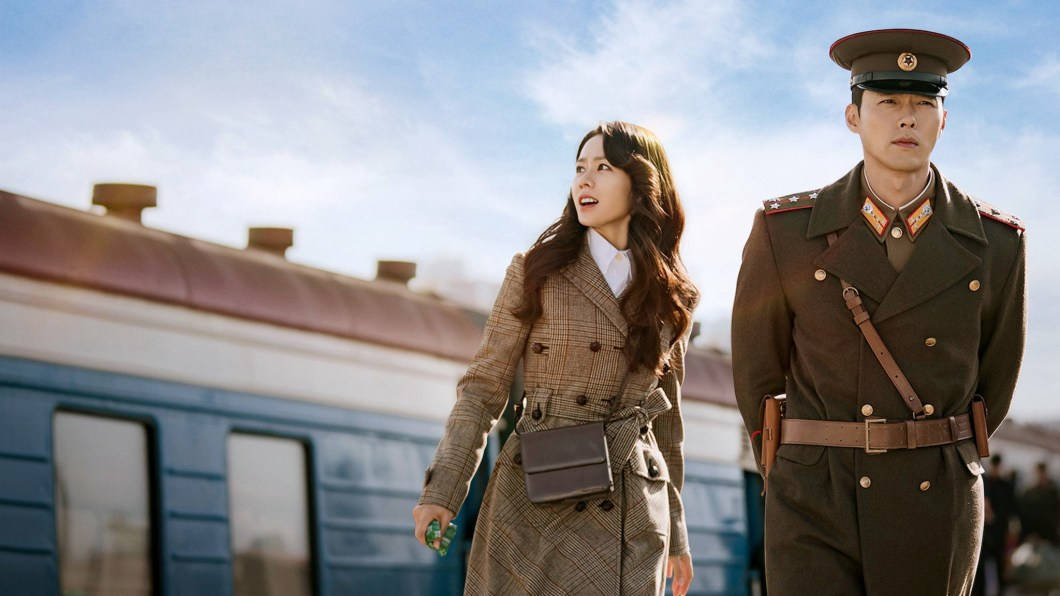 kdrama 桌布 壁紙 — 一位穿著格子外套的女人和一位穿著軍裝的男人站在一輛藍色火車旁，天空明亮。