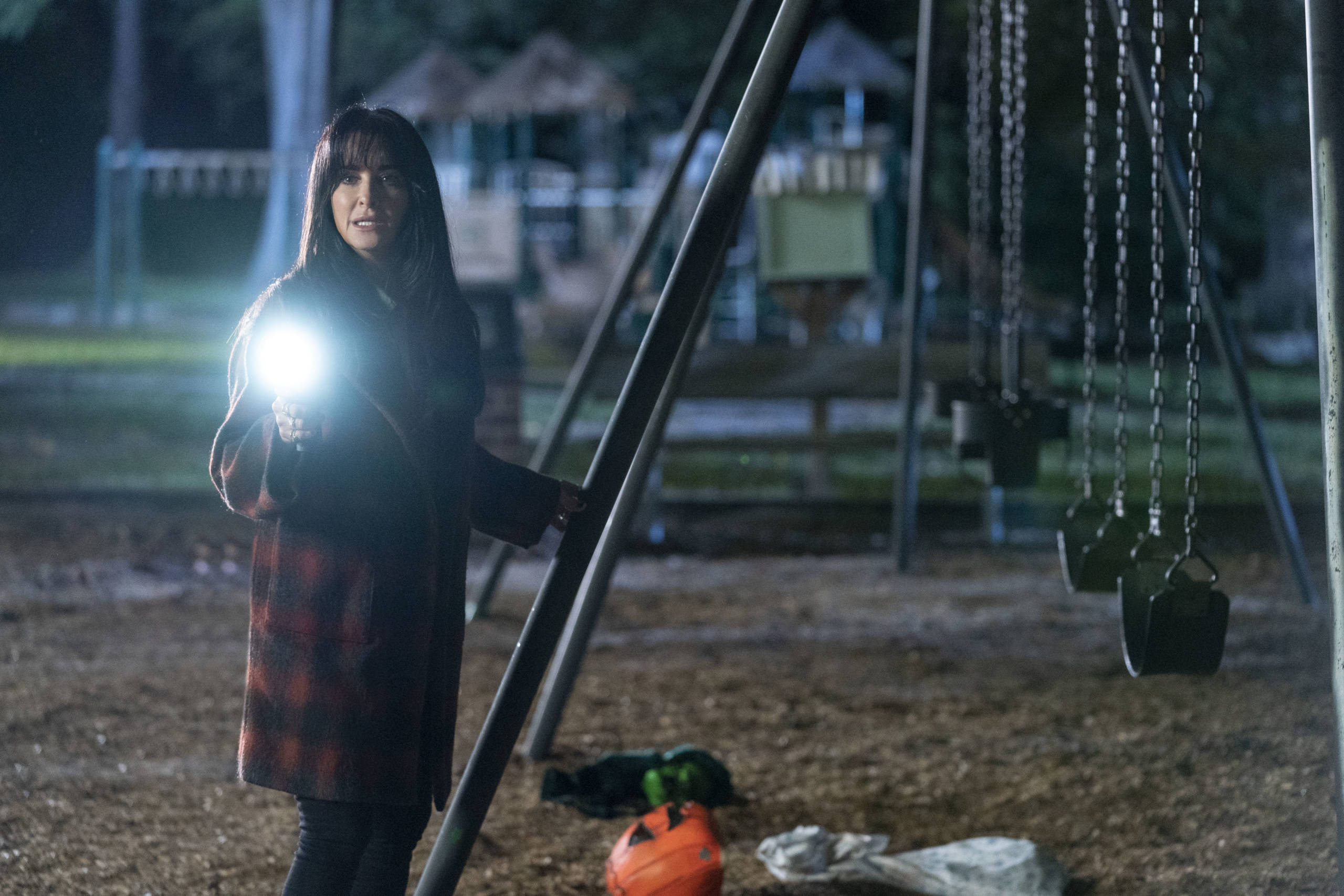 Halloween Kills 桌布 壁紙 — 一位穿著格子外套的女性夜晚站在遊樂場，手持明亮手電筒照亮她的臉。