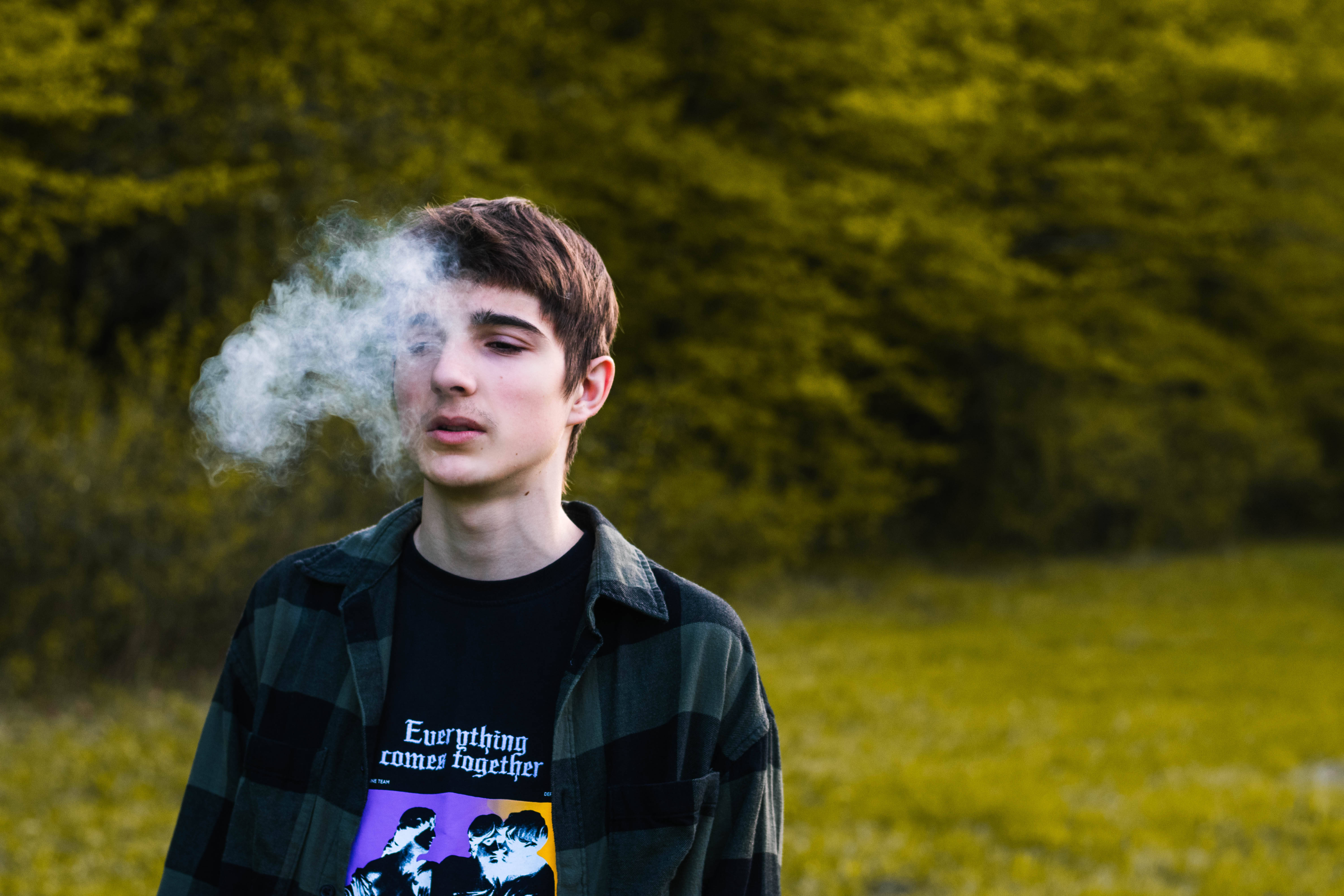 Teenage 桌布 壁紙 — 一位穿著格紋襯衫的年輕男子在充滿活力的綠色森林背景下呼出煙霧。