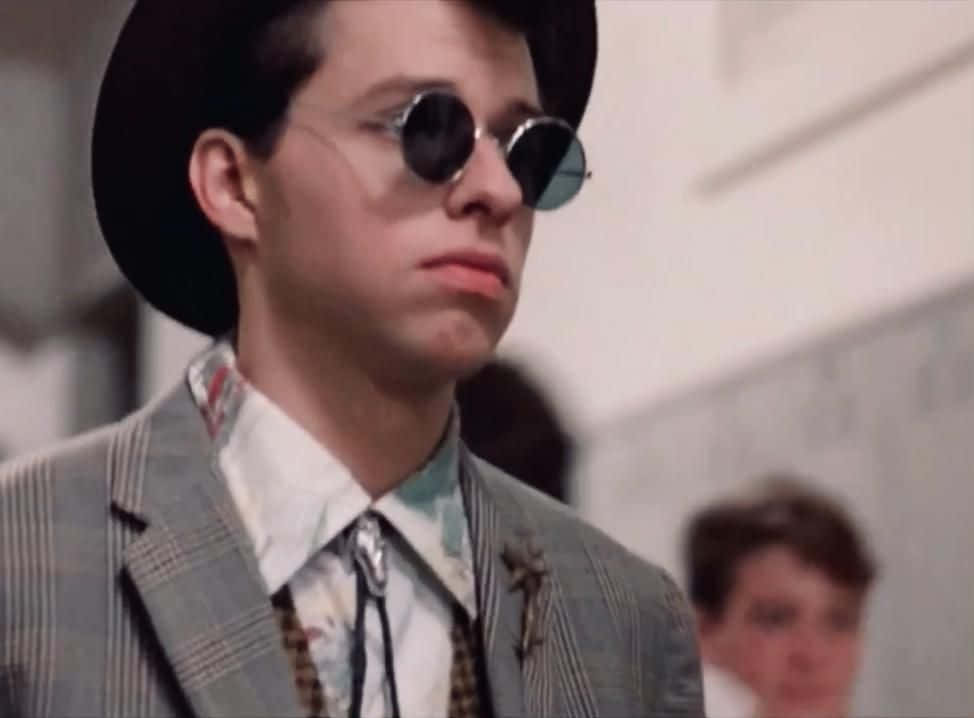 Jon Cryer 桌布 壁紙 — 一位穿著格紋西裝和黑色帽子的年輕男子，戴著圓形太陽眼鏡，室內表情嚴肅。