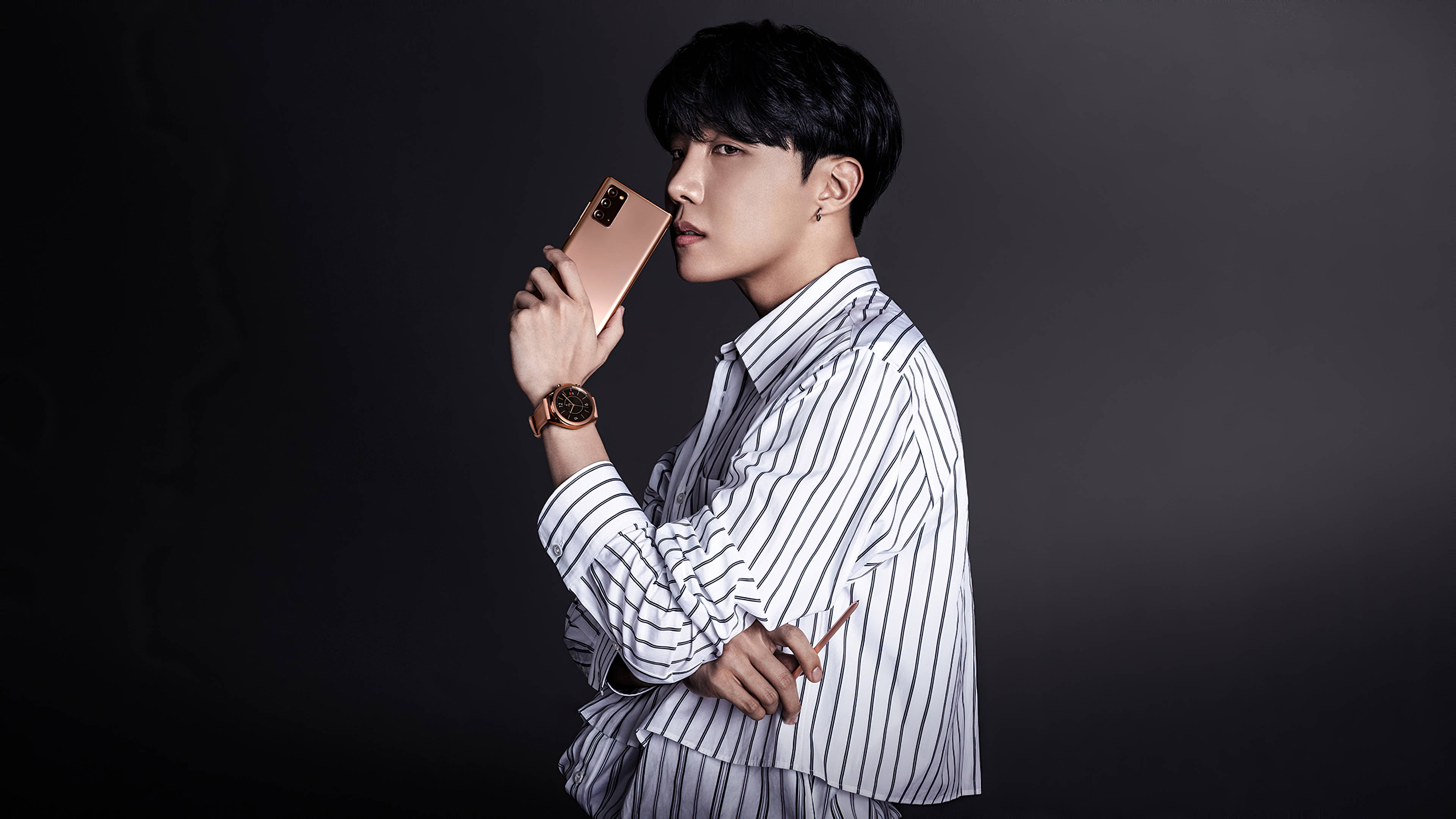美學 BTS 桌布 壁紙 — 一位穿著條紋襯衫的時尚男士在深色漸變背景前拿著玫瑰金色手機。
