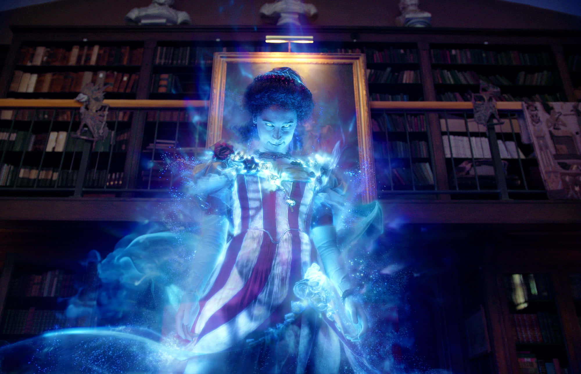 魔鬼剋星 桌布 壁紙 — 一位穿著條紋連衣裙的發光女巫在一個充滿書架的宏偉圖書館中施展魔法。