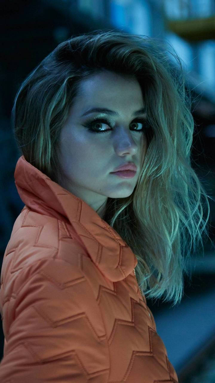 ana de armas 桌布 壁紙 — 一位穿著橙色絎縫外套的女性在冷藍色燈光下，頭髮凌亂，凝視著。