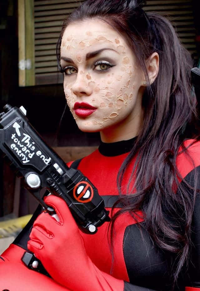 Lady Deadpool 桌布 壁紙 — 一位穿著死侍服裝並帶有臉部彩繪的女性，手持道具槍，直視鏡頭。