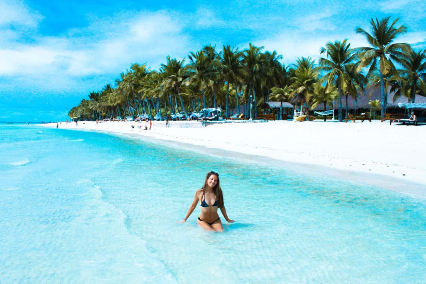 Travel Desktop 桌布 壁紙 — 一位穿著比基尼的女性在清澈碧綠的海水中微笑涉水，旁邊是白色沙灘，棕櫚樹成行，頭頂是明亮的藍天。