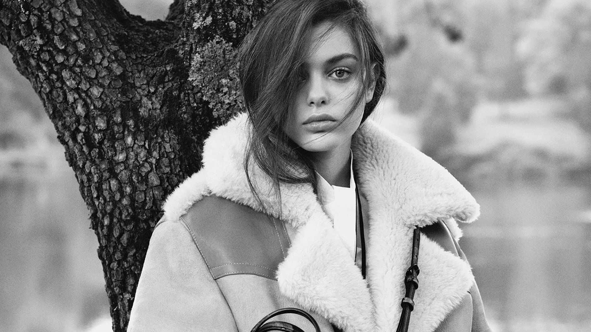 Odeya Rush 桌布 壁紙 — 一位穿著毛絨外套的女性，在單色戶外人像中靠著紋理豐富的樹幹。