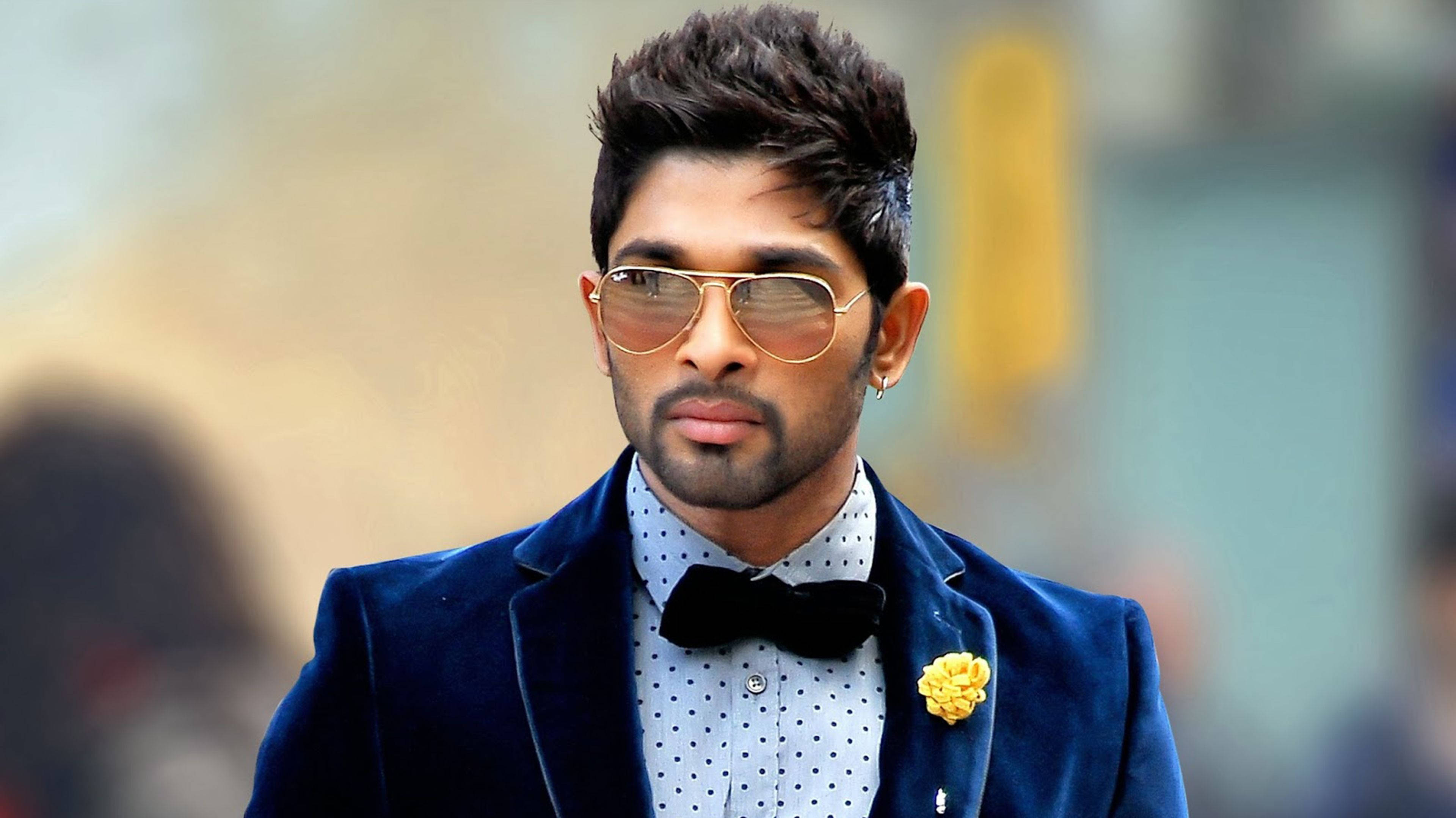 Allu Arjun 桌布 壁紙 — 一位穿著海軍藍天鵝絨西裝外套和金色邊框太陽眼鏡的時尚男士，佩戴黃色襟花，散發自信。