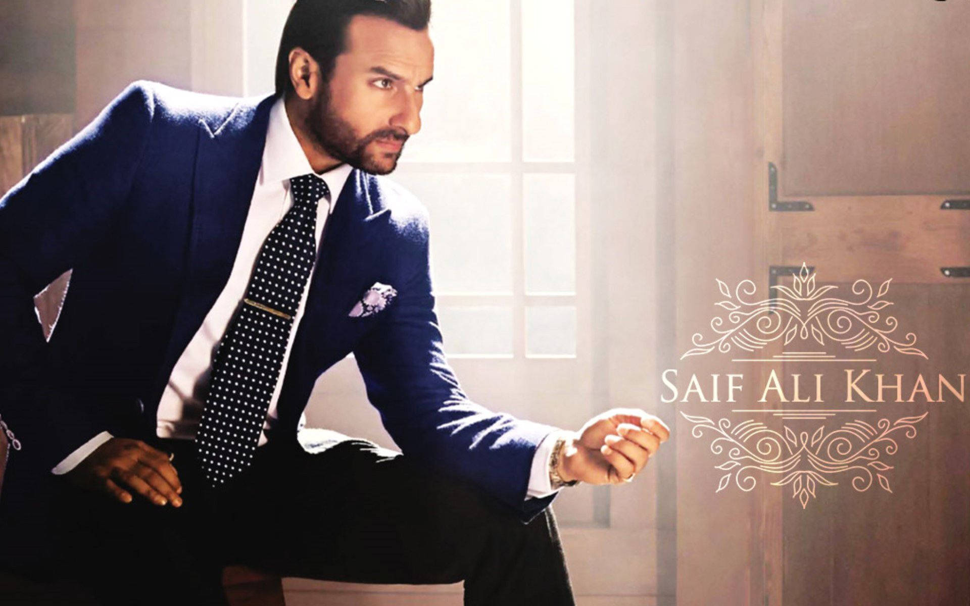 Saif Ali Khan 桌布 壁紙 — 一位穿著海軍藍西裝、衣著講究的男子自信地坐在窗邊，旁邊有華麗的金色字樣。