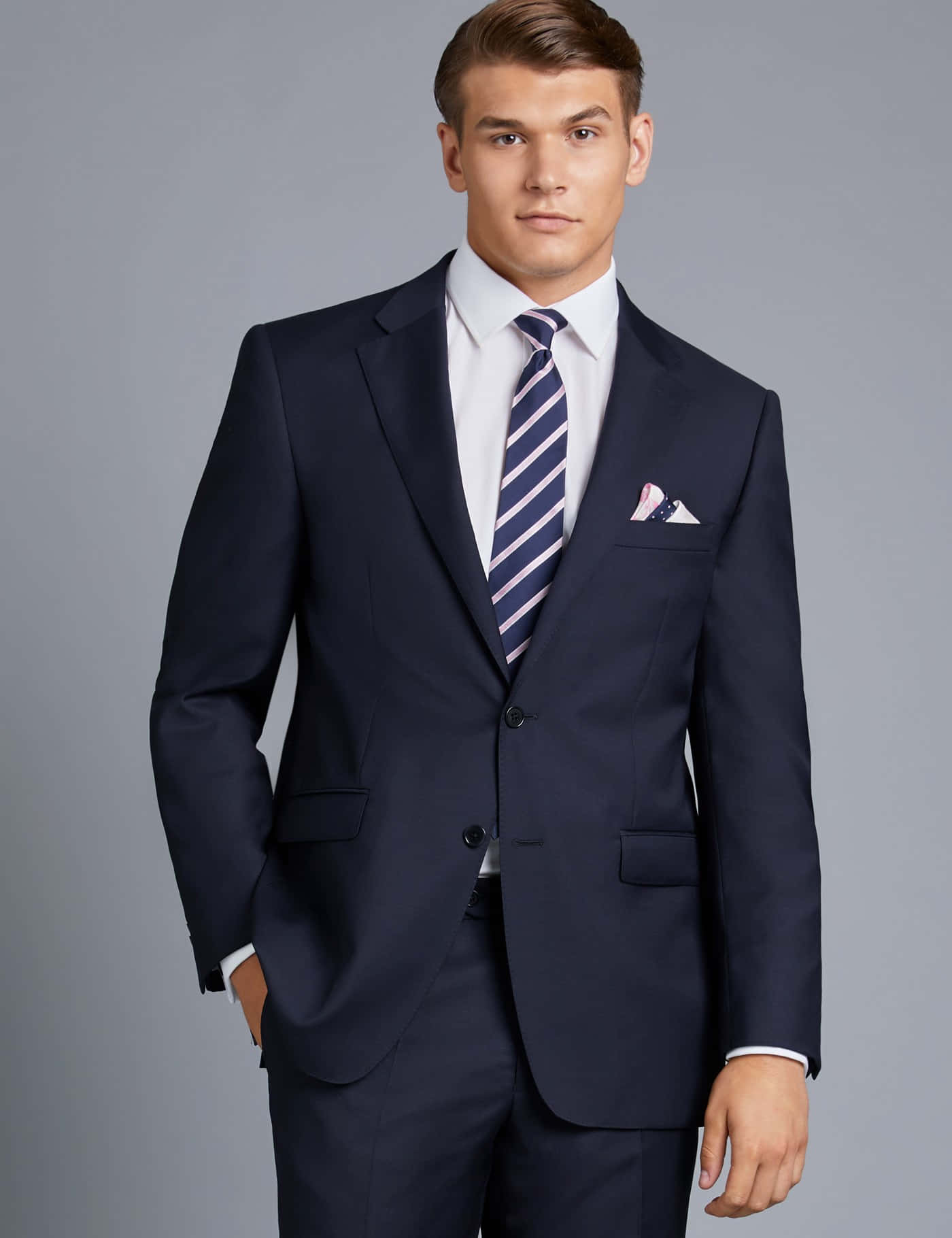 suit 桌布 壁紙 — 一位穿著海軍藍西裝搭配條紋領帶的時尚男士，自信地站在中性灰色背景前。