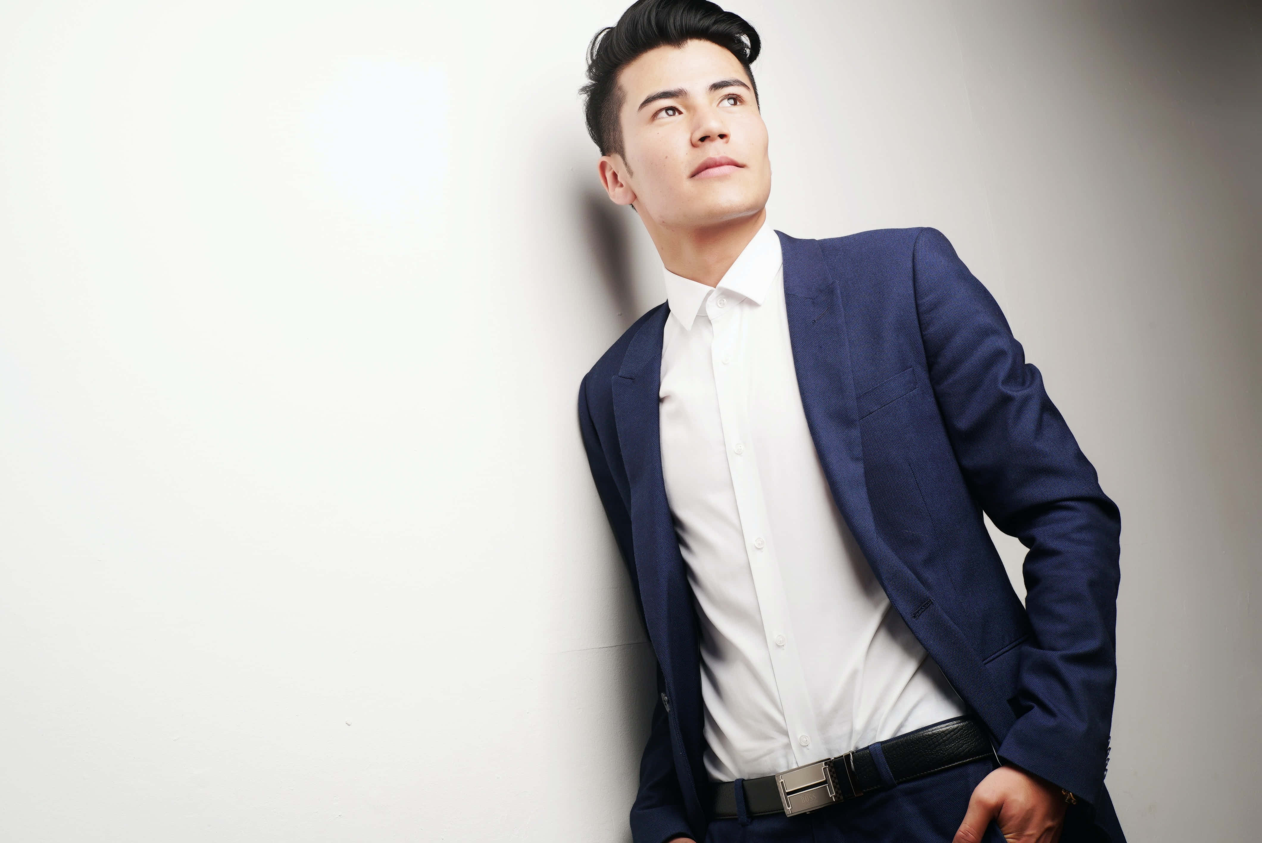 Navy Blue Suit 桌布 壁紙 — 一位穿著海軍藍西裝的時尚男士靠著素牆，自信地向上凝視。