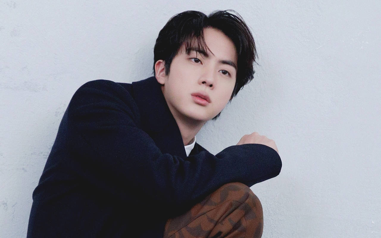 kim seok jin 桌布 壁紙 — 一位穿著深色毛衣的年輕男子，靠著紋理白色牆壁，神情若有所思。