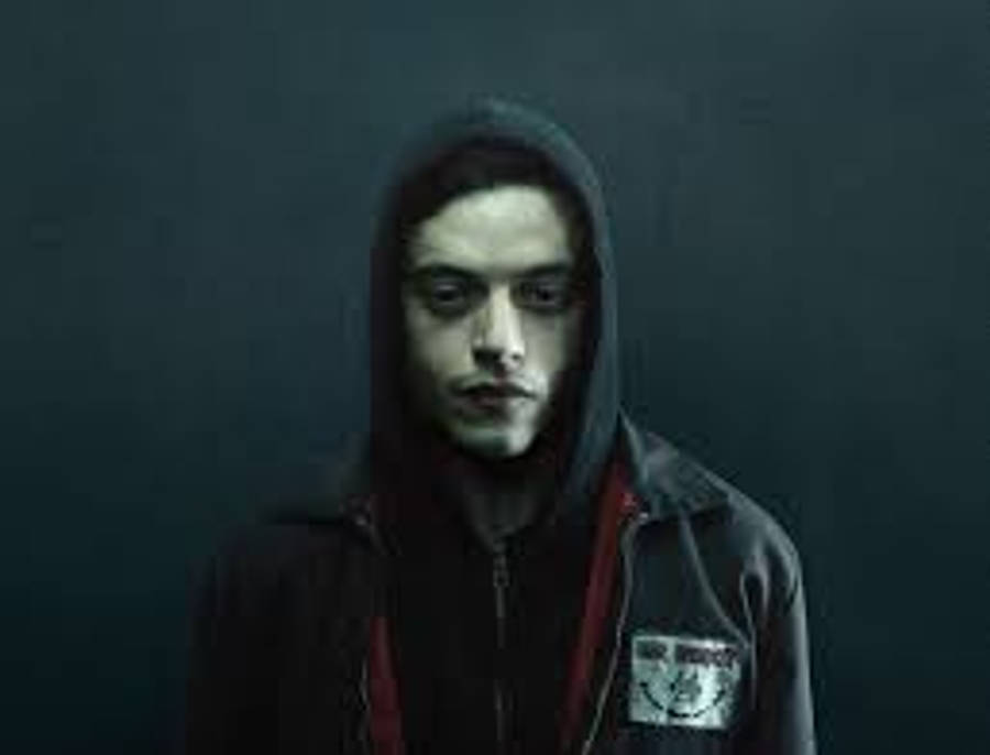 Rami Malek 桌布 壁紙 — 一位穿著深色連帽衫的年輕男子在柔和灰色背景和戲劇性燈光下強烈凝視。