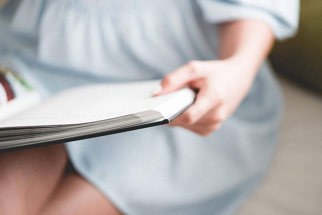 Education 桌布 壁紙 — 一位穿著淺藍色條紋連衣裙的人，專注地拿著一本打開的書，背景柔和模糊。