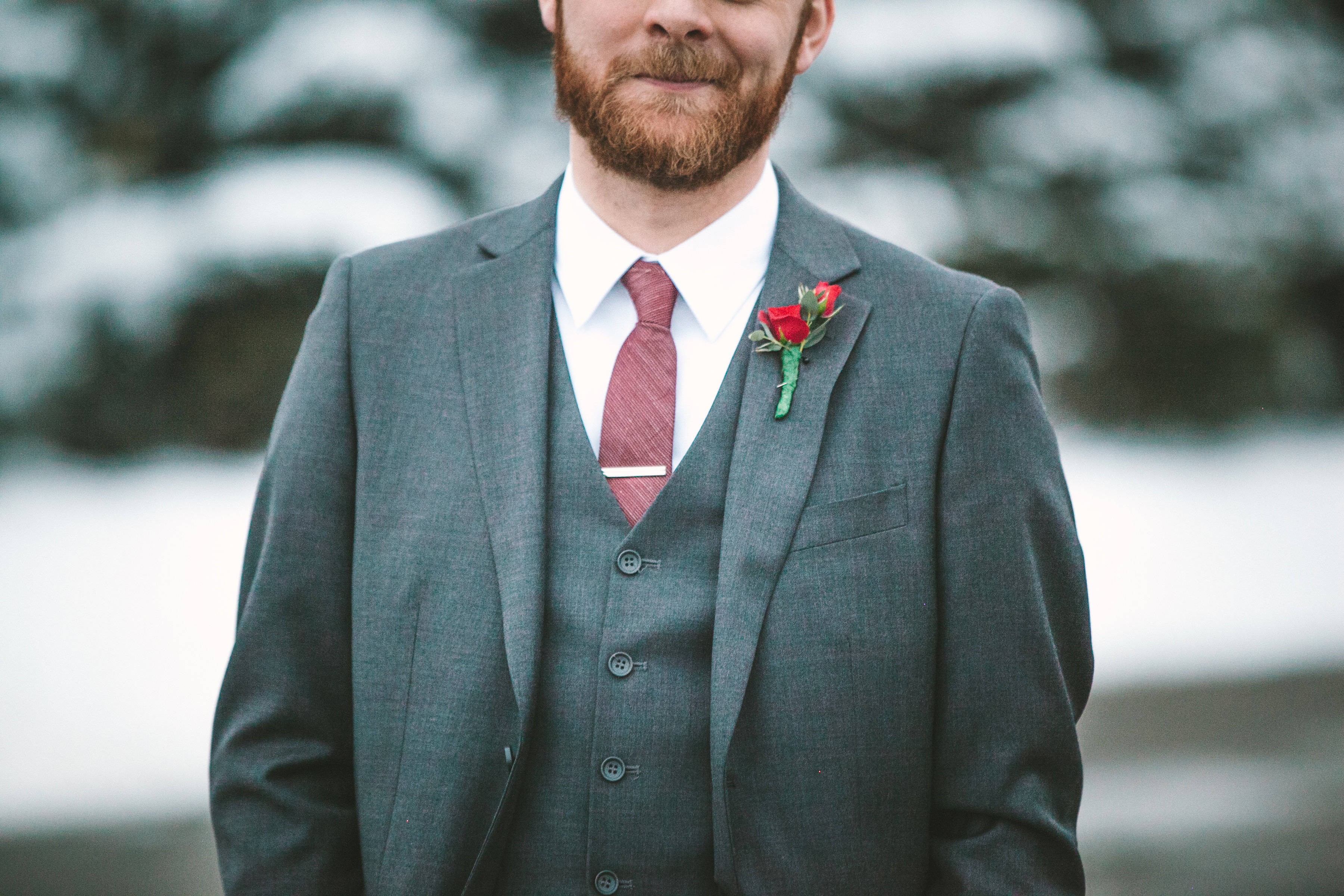 Groom 桌布 壁紙 — 一位穿著灰色三件套西裝、佩戴紅色玫瑰胸花的新郎站在雪白的冬季背景下。