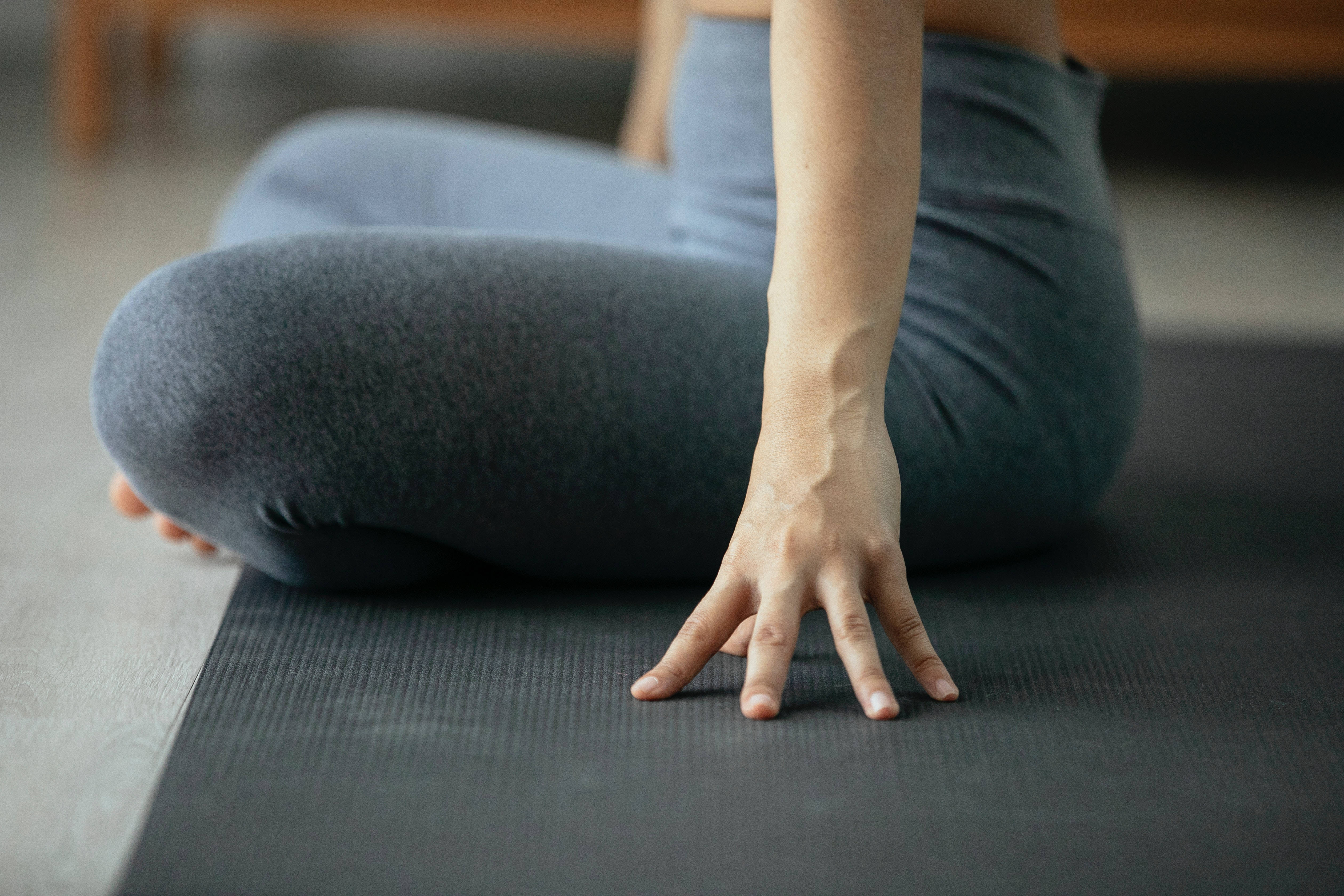 Exercise 桌布 壁紙 — 一位穿著灰色緊身褲的人盤腿坐在黑色瑜伽墊上，一隻手放在表面。