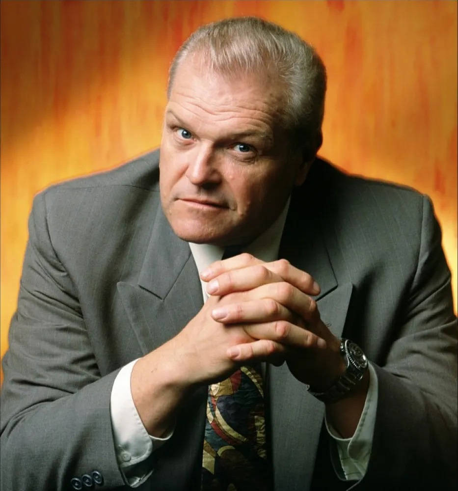 suit 桌布 壁紙 — 一位穿著灰色西裝和圖案領帶的嚴肅男子，在溫暖的橙色漸變背景前雙手合十擺姿勢。