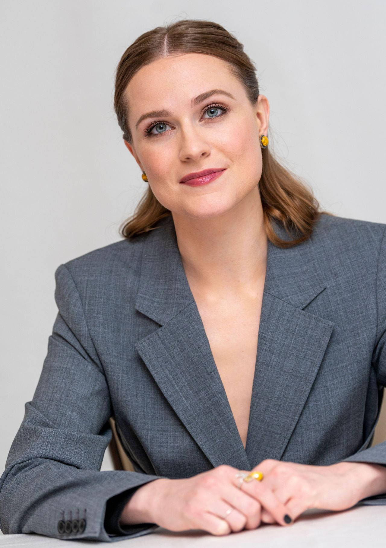 Celebrity 桌布 壁紙 — 一位穿著灰色西裝外套的優雅女性，坐在白色背景的桌子旁，露出溫柔的微笑。