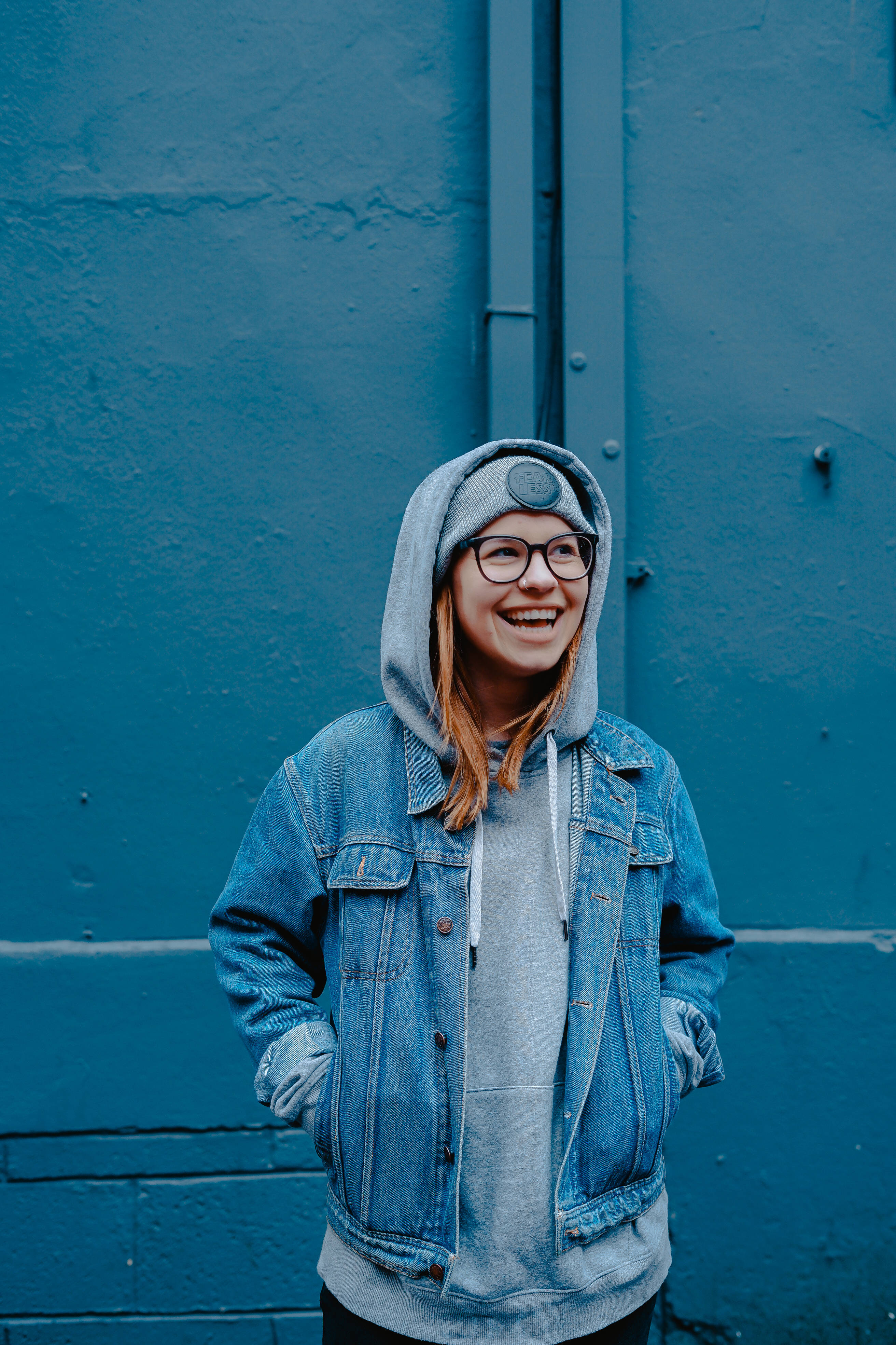 Brave 桌布 壁紙 — 一位穿著牛仔外套和連帽衫的開朗年輕女子，在帶有紋理的藍色牆壁前燦爛地笑著。