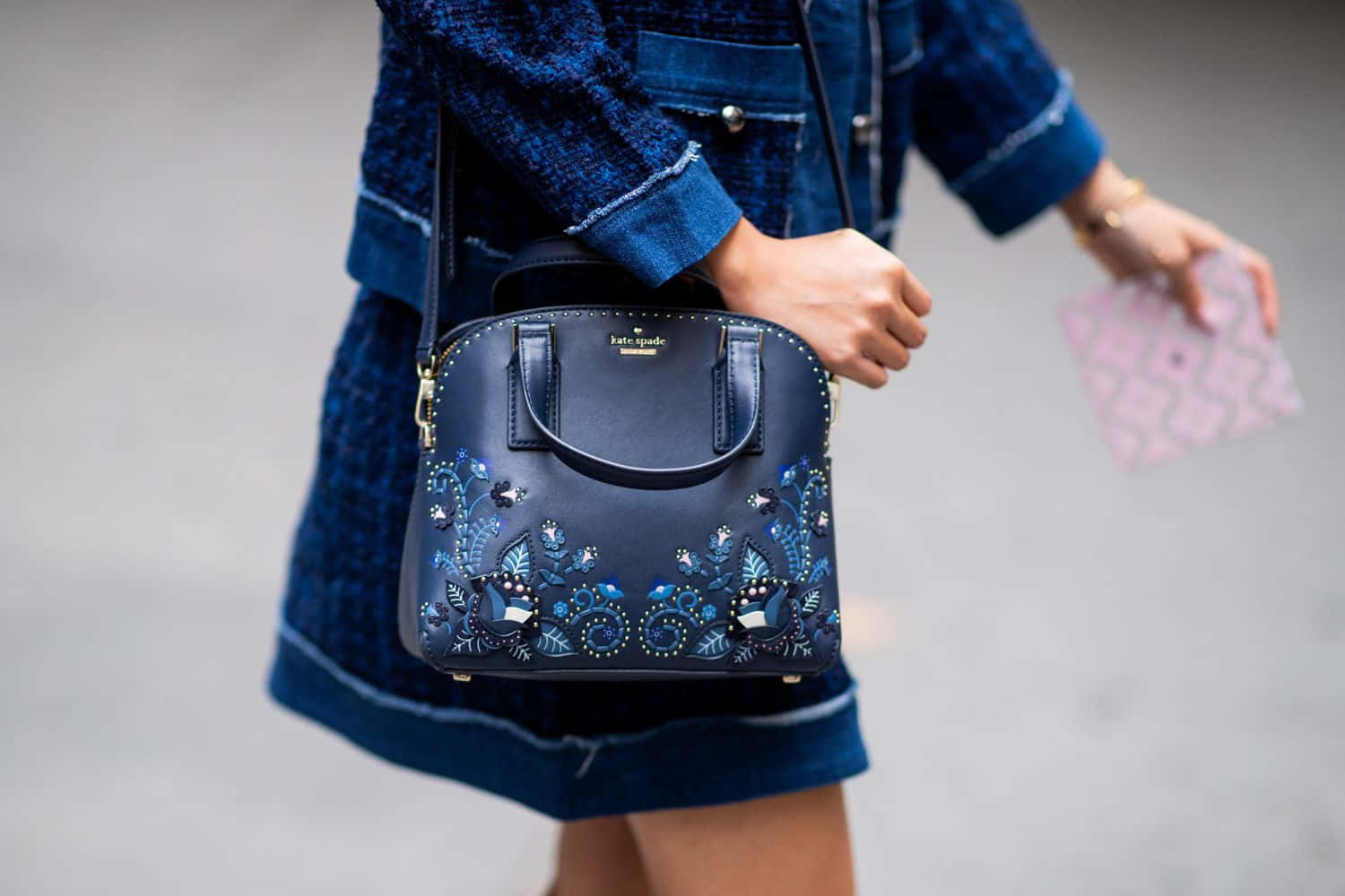 Kate Spade 桌布 壁紙 — 一位穿著牛仔布的人拿著一個深藍色飾有花卉珠寶的手袋和一個粉紅色圖案的手拿包。