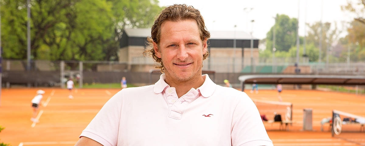 Tennis 桌布 壁紙 — 一位穿著白色Polo衫的微笑男子站在橙色紅土網球場上，背景有球員。