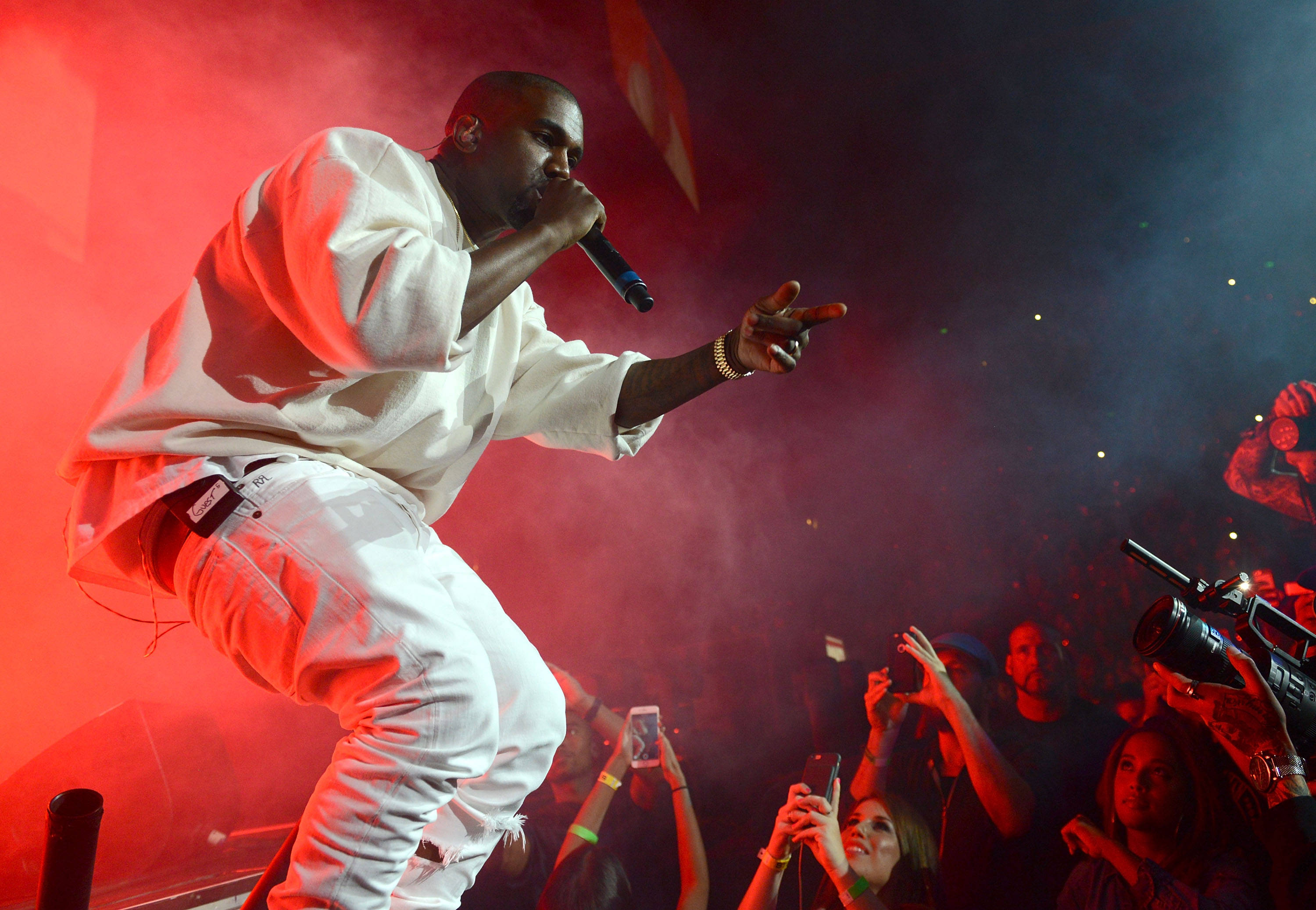 Kanye 桌布 壁紙 — 一位穿著白色服裝的饒舌歌手在紅色燈光下於舞台上充滿活力地表演，下方有群眾歡呼。