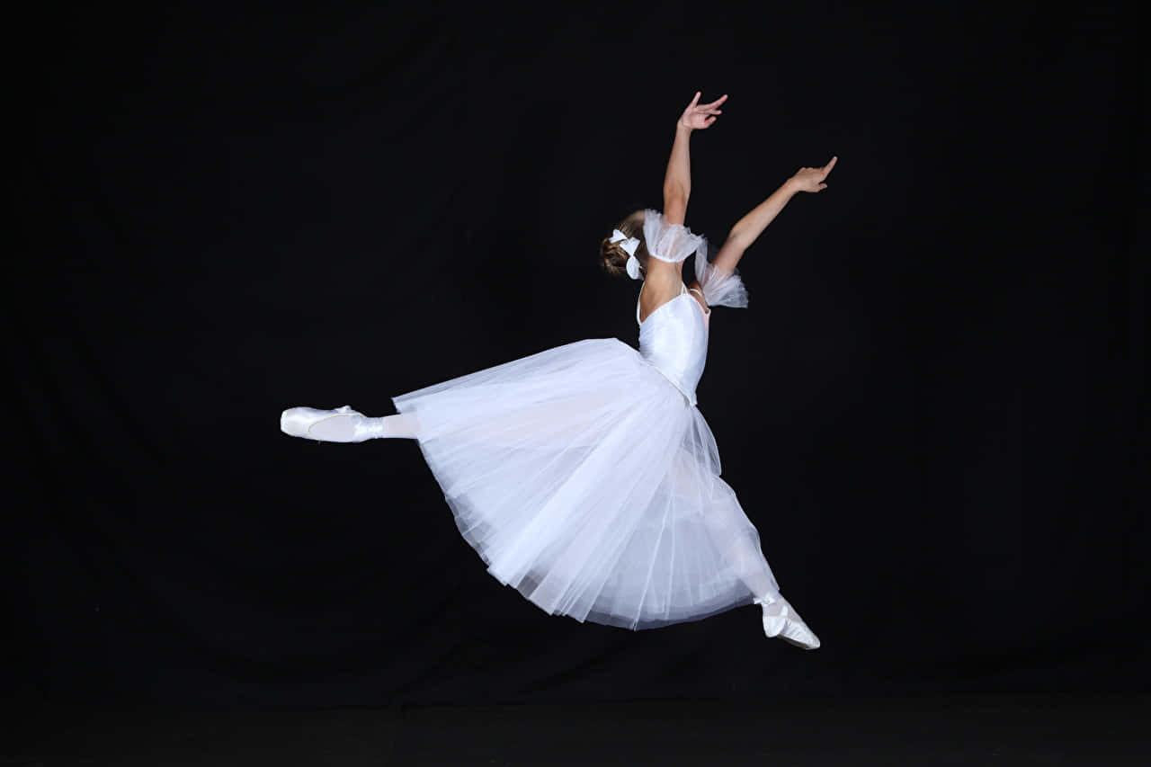 Ballet 桌布 壁紙 — 一位穿著白色芭蕾舞裙的芭蕾舞者，在純黑背景下優雅躍起，雙臂伸展，姿態優美。