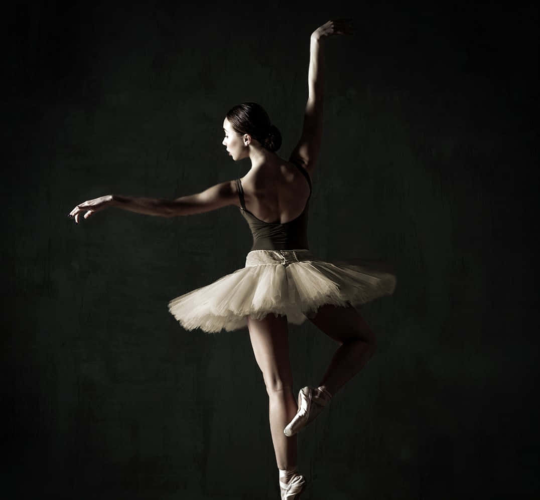 ballerina 桌布 壁紙 — 一位穿著白色芭蕾舞裙的芭蕾舞者，在深色紋理背景上優雅地躍起，戲劇性的燈光凸顯了她的身形。