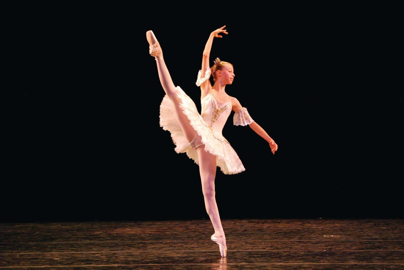 Ballet Dancer 桌布 壁紙 — 一位穿著白色芭蕾舞裙的芭蕾舞者，在黑暗的舞台背景下以足尖優雅地表演阿拉貝斯克。