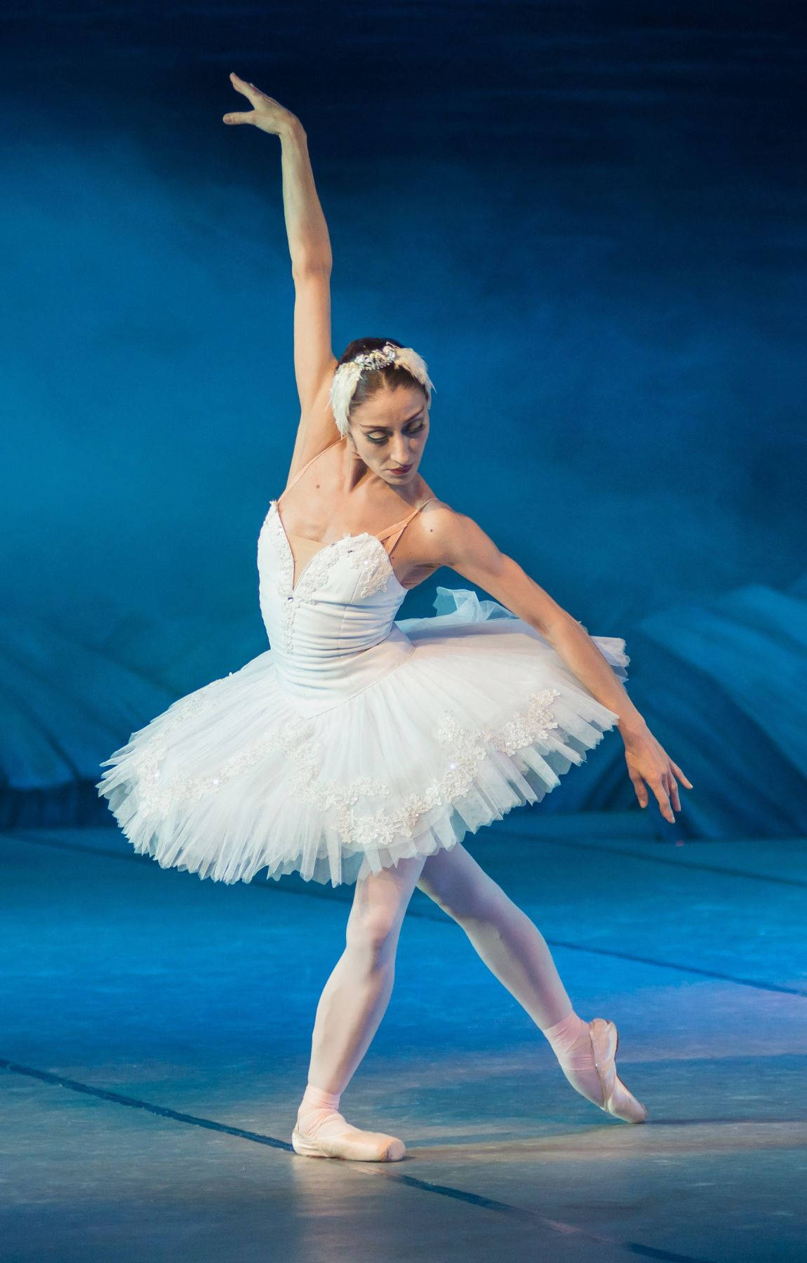 Ballet 桌布 壁紙 — 一位穿著白色芭蕾舞裙的芭蕾舞者在戲劇性的藍色舞台燈光下優雅地踮起腳尖擺姿勢。