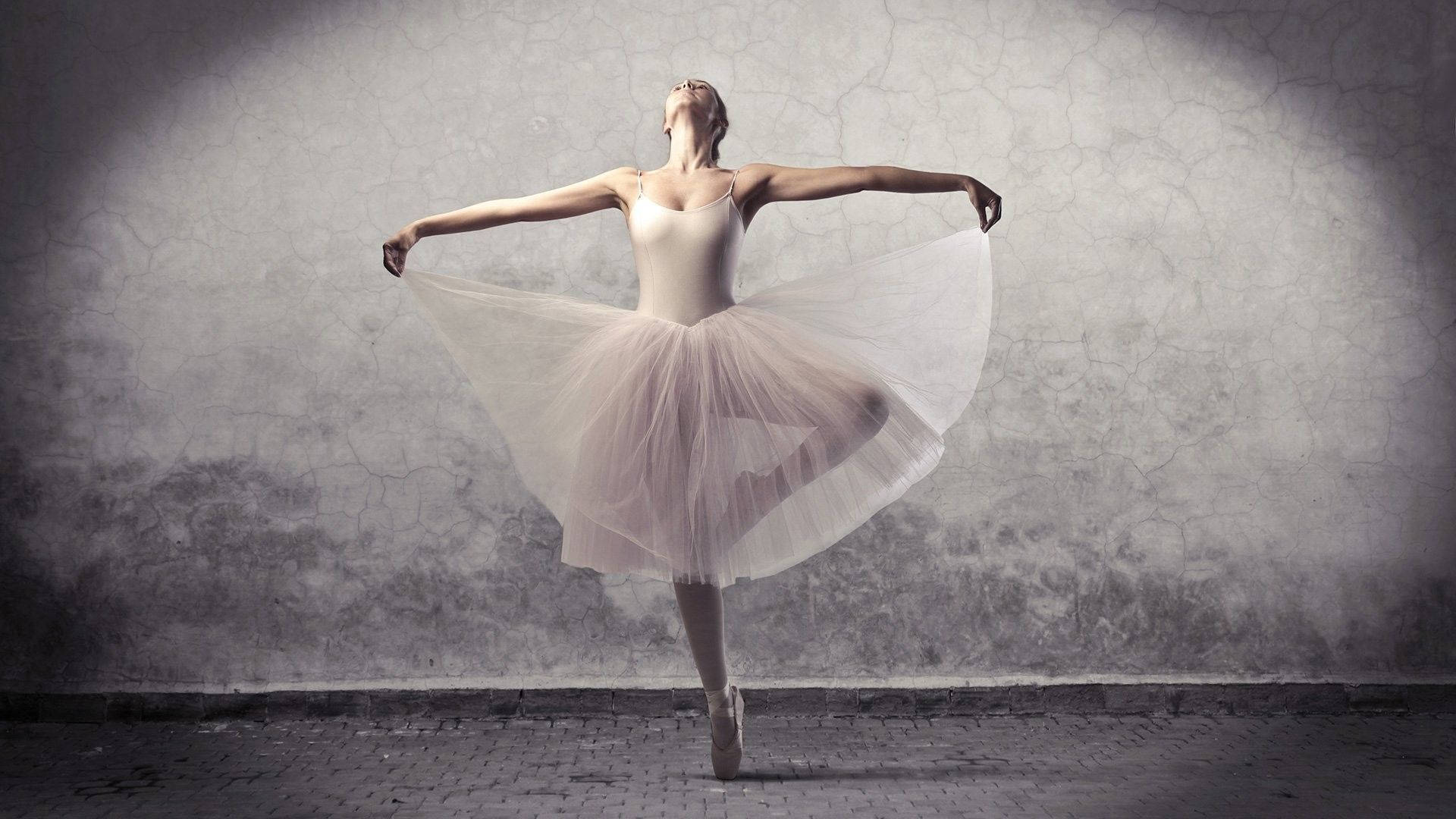 Ballet 桌布 壁紙 — 一位穿著白色芭蕾舞裙的芭蕾舞者在戲劇性的聚光燈下，在破裂的灰色牆壁前優雅地跳躍。