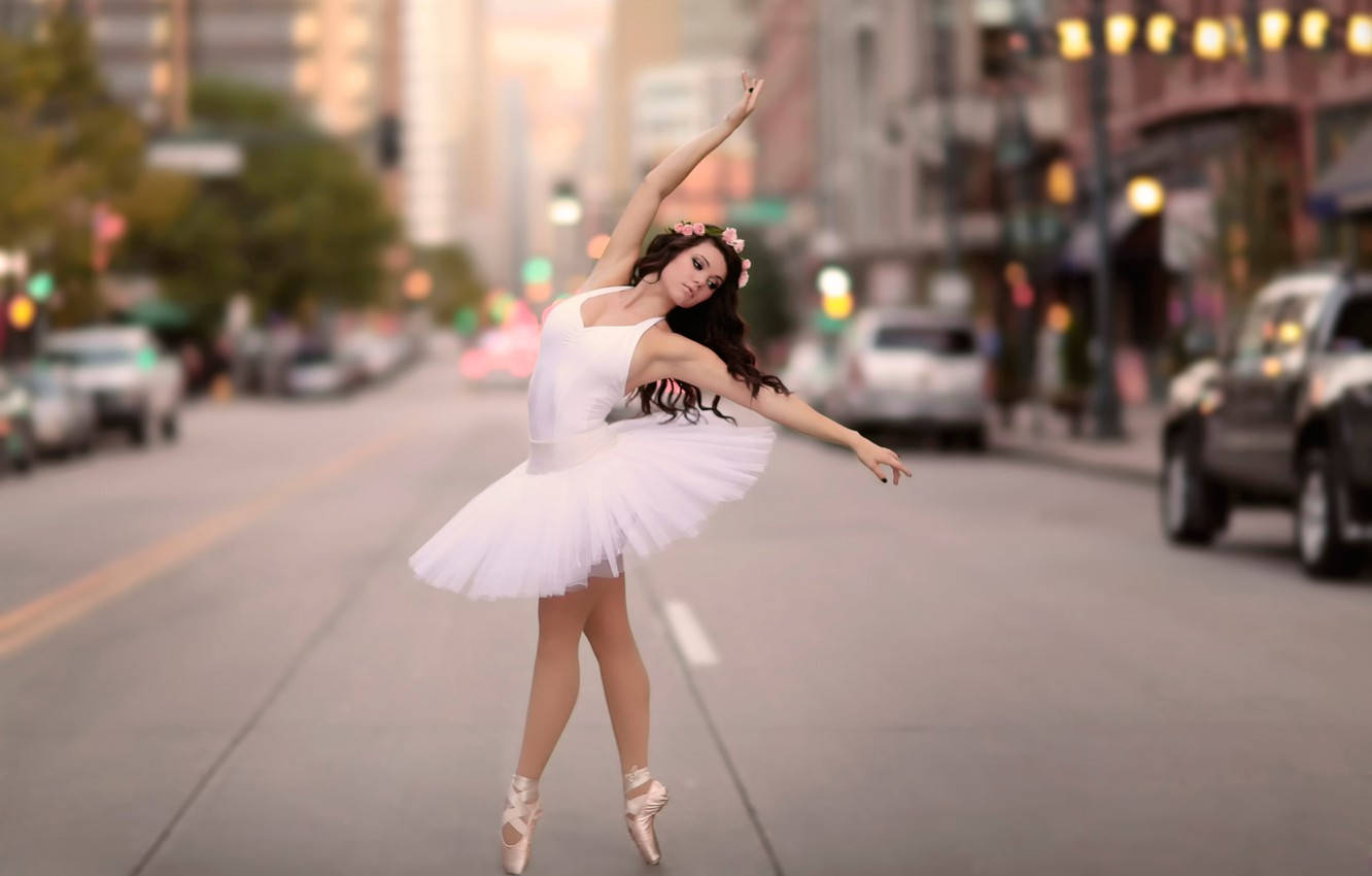 Ballet 桌布 壁紙 — 一位穿著白色芭蕾舞裙的芭蕾舞者在黃金時刻的模糊城市街道上優雅地踮起腳尖擺姿勢。