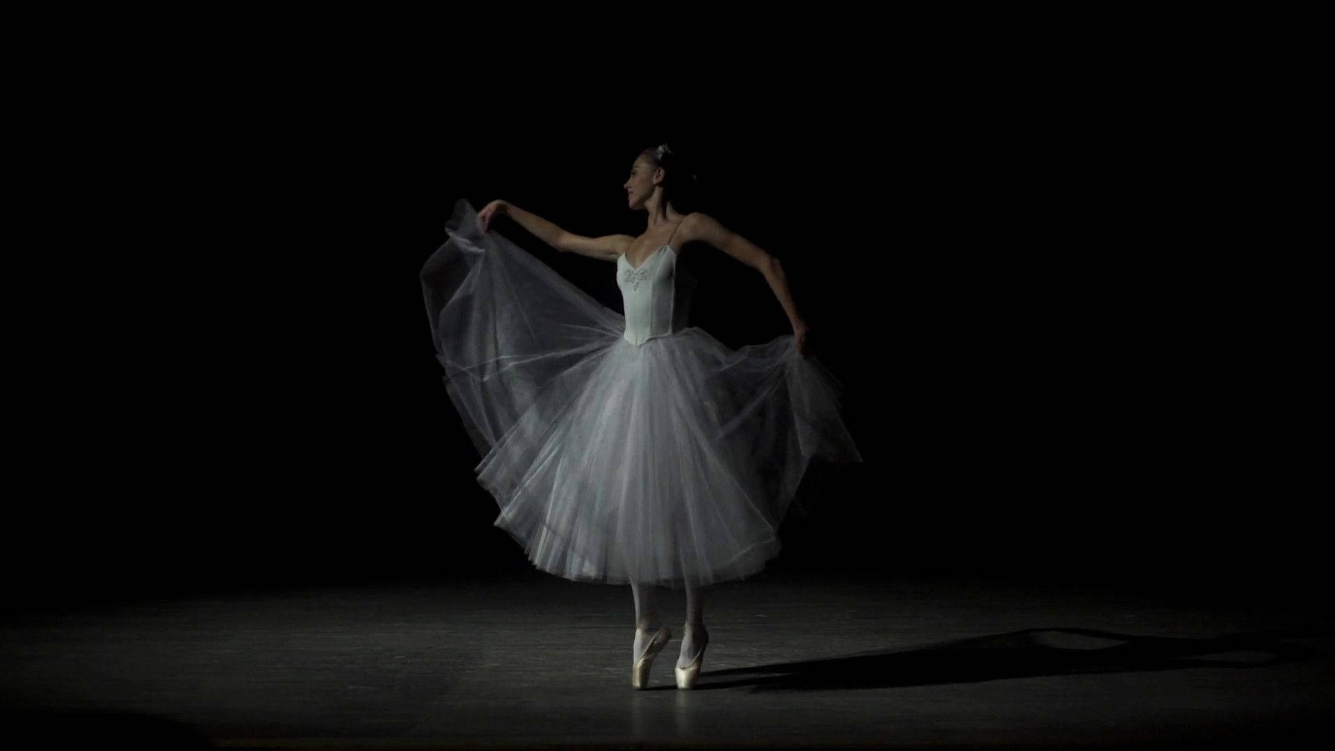 dancer 桌布 壁紙 — 一位穿著白色芭蕾舞裙的芭蕾舞者在黑色舞台上的聚光燈下優雅地旋轉。