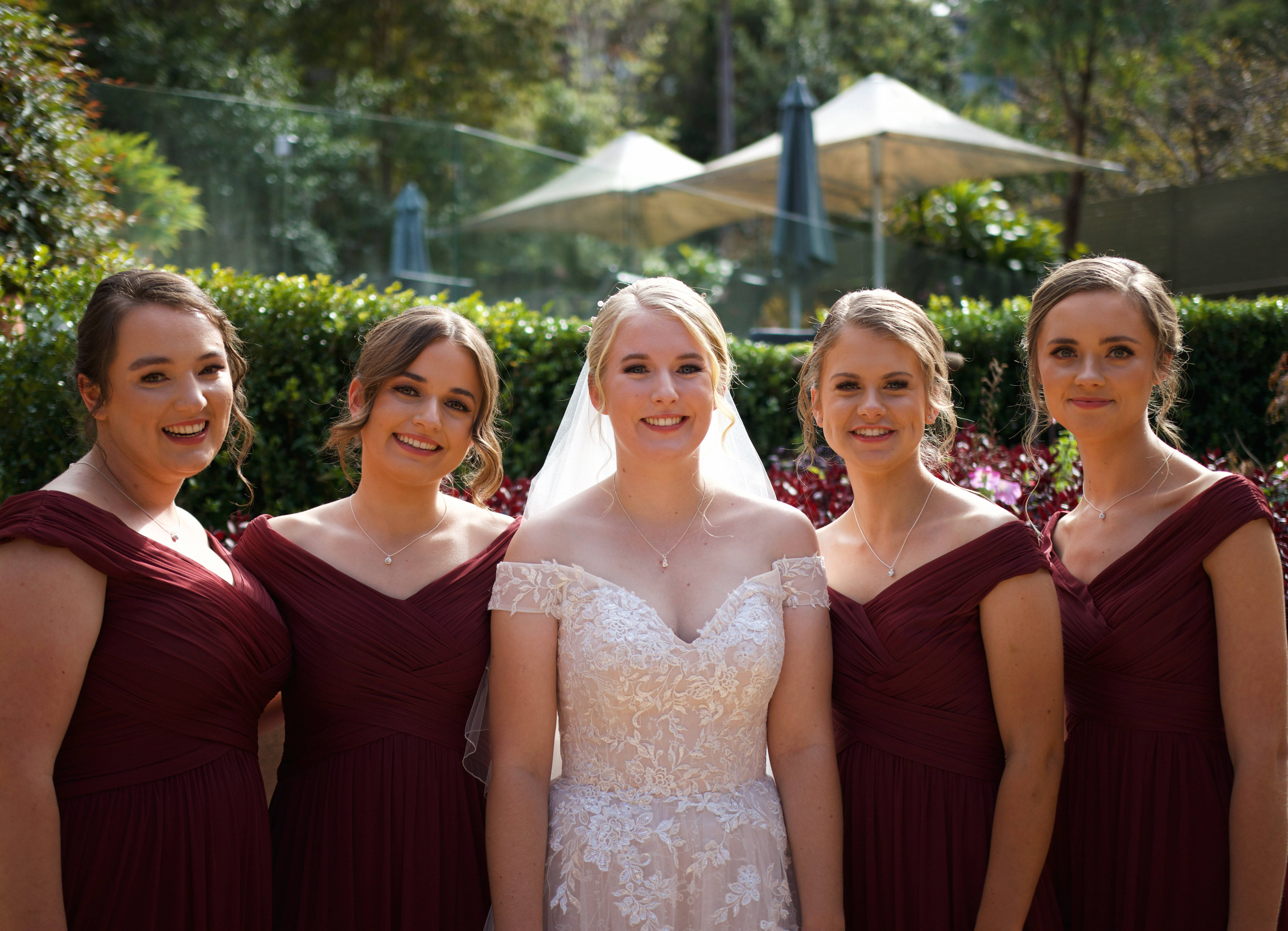 Bridesmaids 桌布 壁紙 — 一位穿著白色蕾絲婚紗的新娘與四位穿著相配酒紅色禮服的伴娘在戶外微笑。