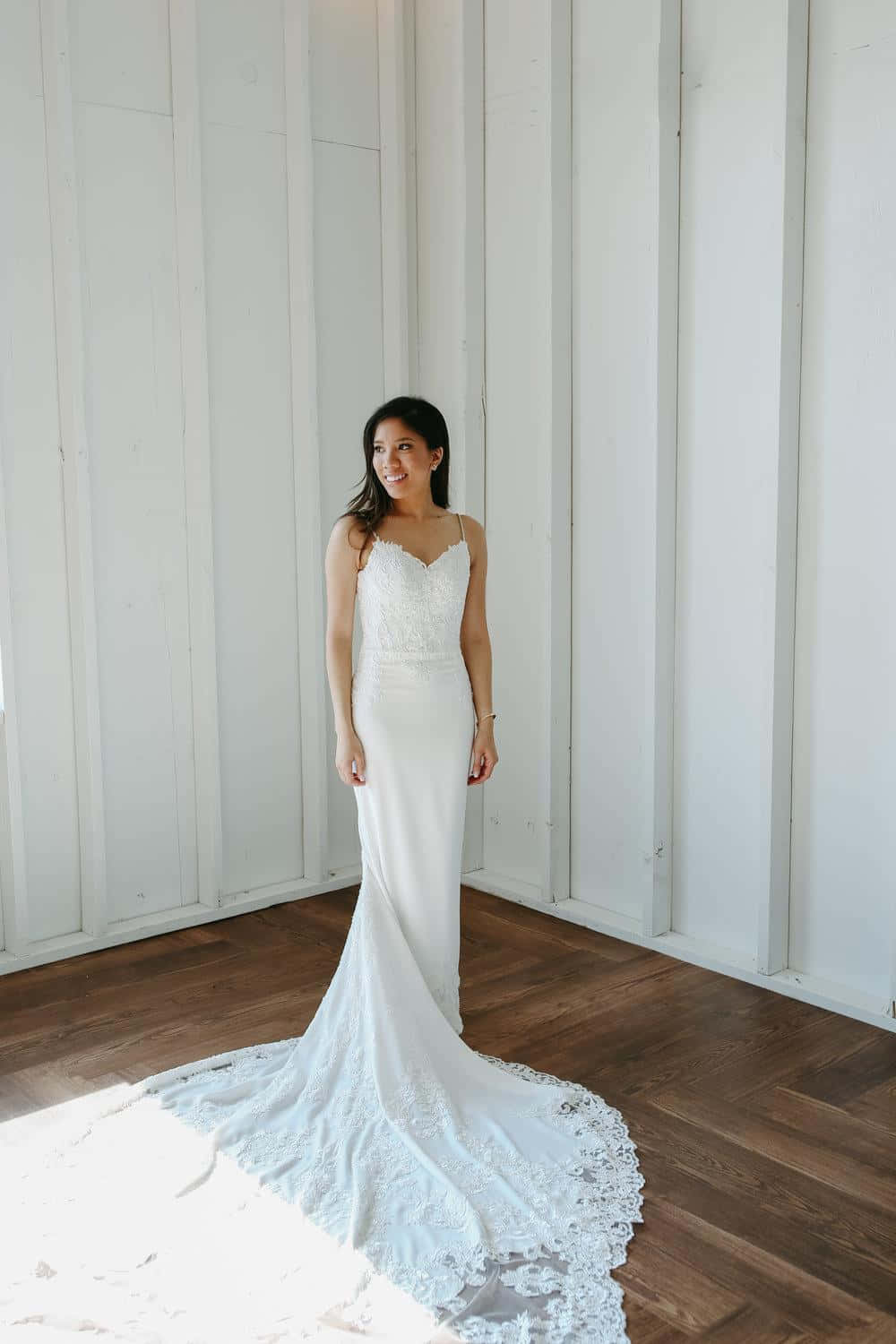 Bride's Dress 桌布 壁紙 — 一位穿著白色蕾絲美人魚婚紗的新娘，在明亮的白色鑲板牆和木地板上溫柔地微笑。