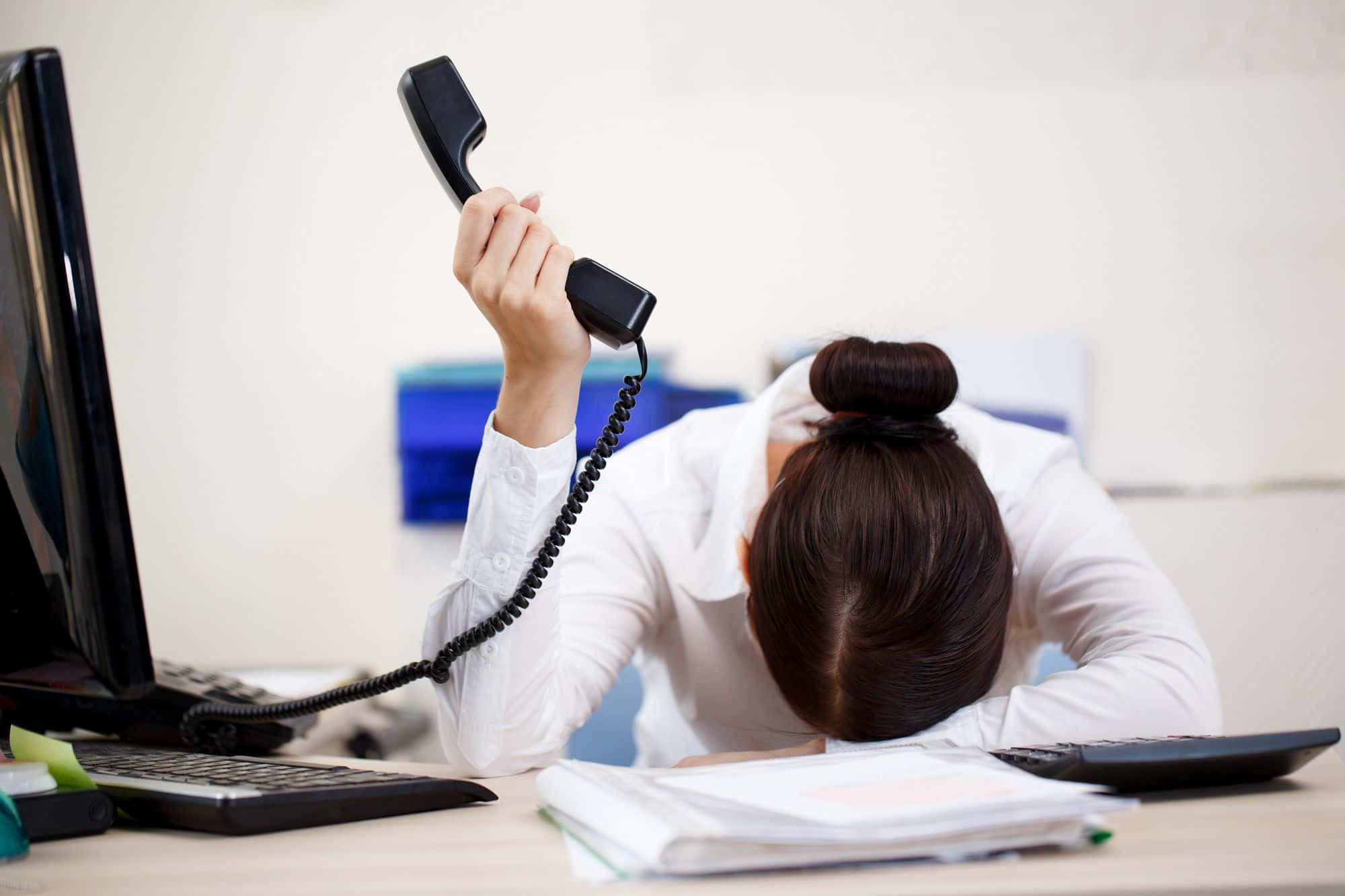 Telemarketing 桌布 壁紙 — 一位穿著白色襯衫的壓力大的辦公室職員癱倒在辦公桌上，沮喪地高舉著黑色電話聽筒。